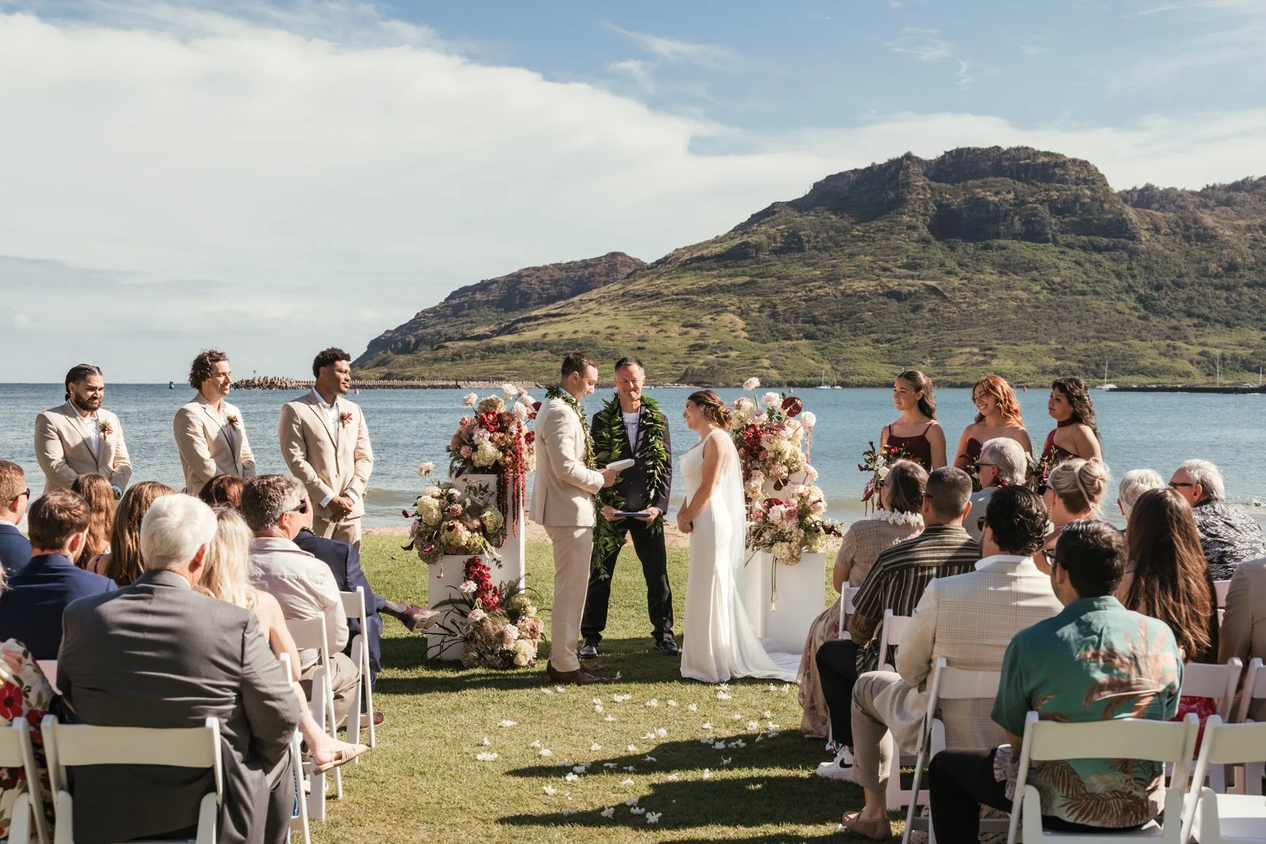 Wedding ceremony on the oceanfront lawn at the Royal Sonesta Kauai Resort in Lihue, with guests, wedding party and Kalapaki Bay mountains behind