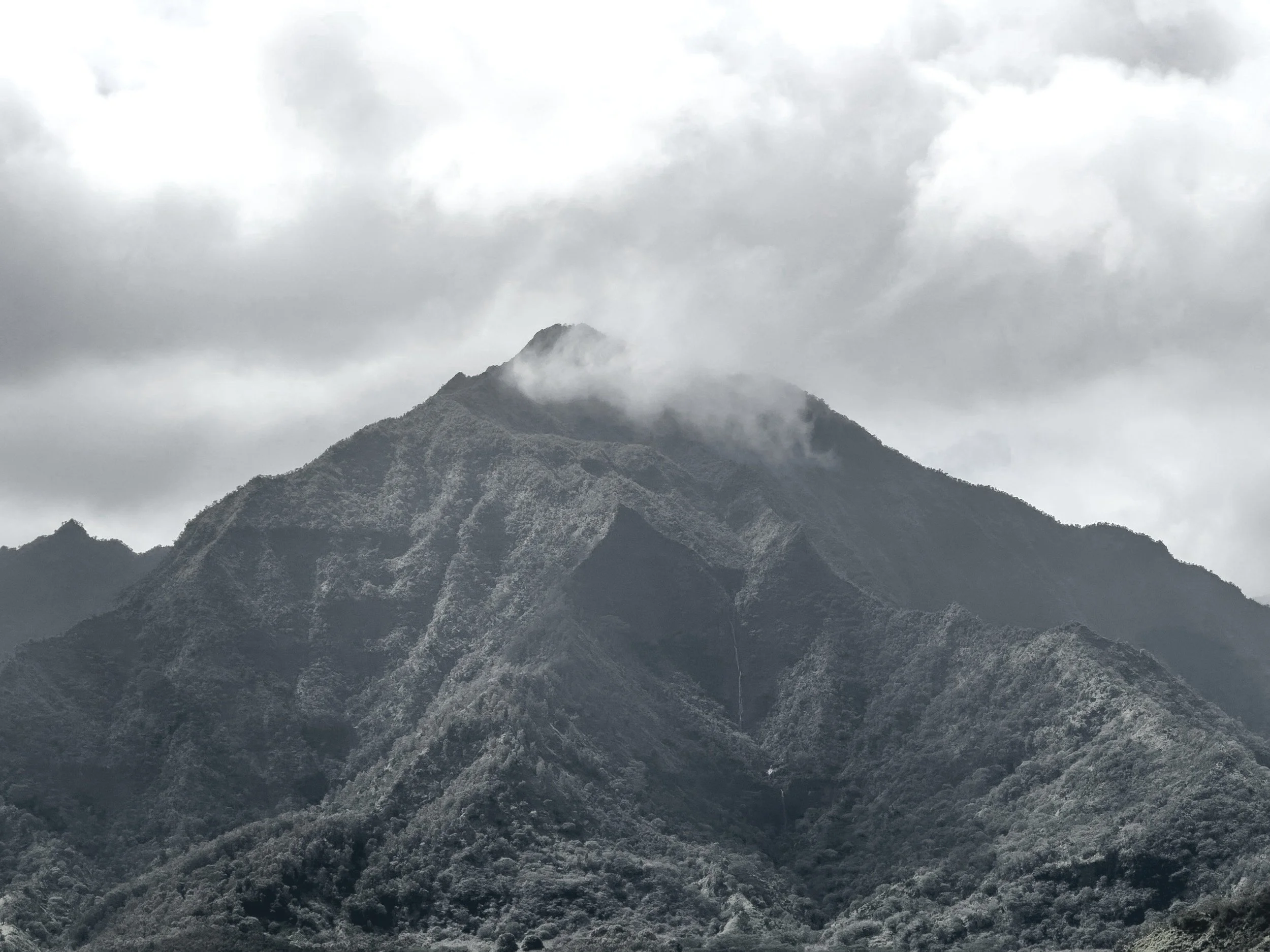 A mountain with cloudy sky and some clouds partially covering its peaks.