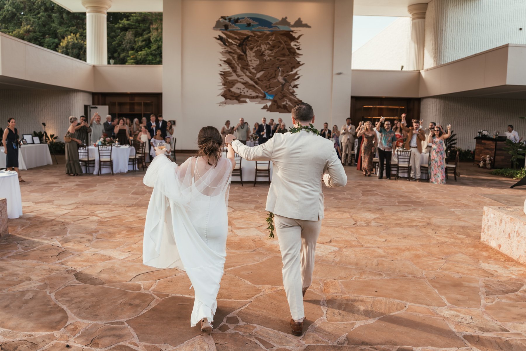 Bride and groom raising their joined hands as wedding guests cheer during their grand entrance at Puna Court, Royal Sonesta Kauai Resort in Lihue