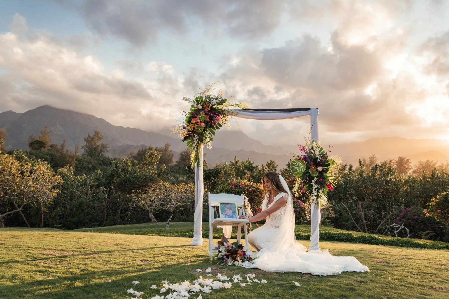 Bride with picture of mother under wedding arch after wedding ceremony