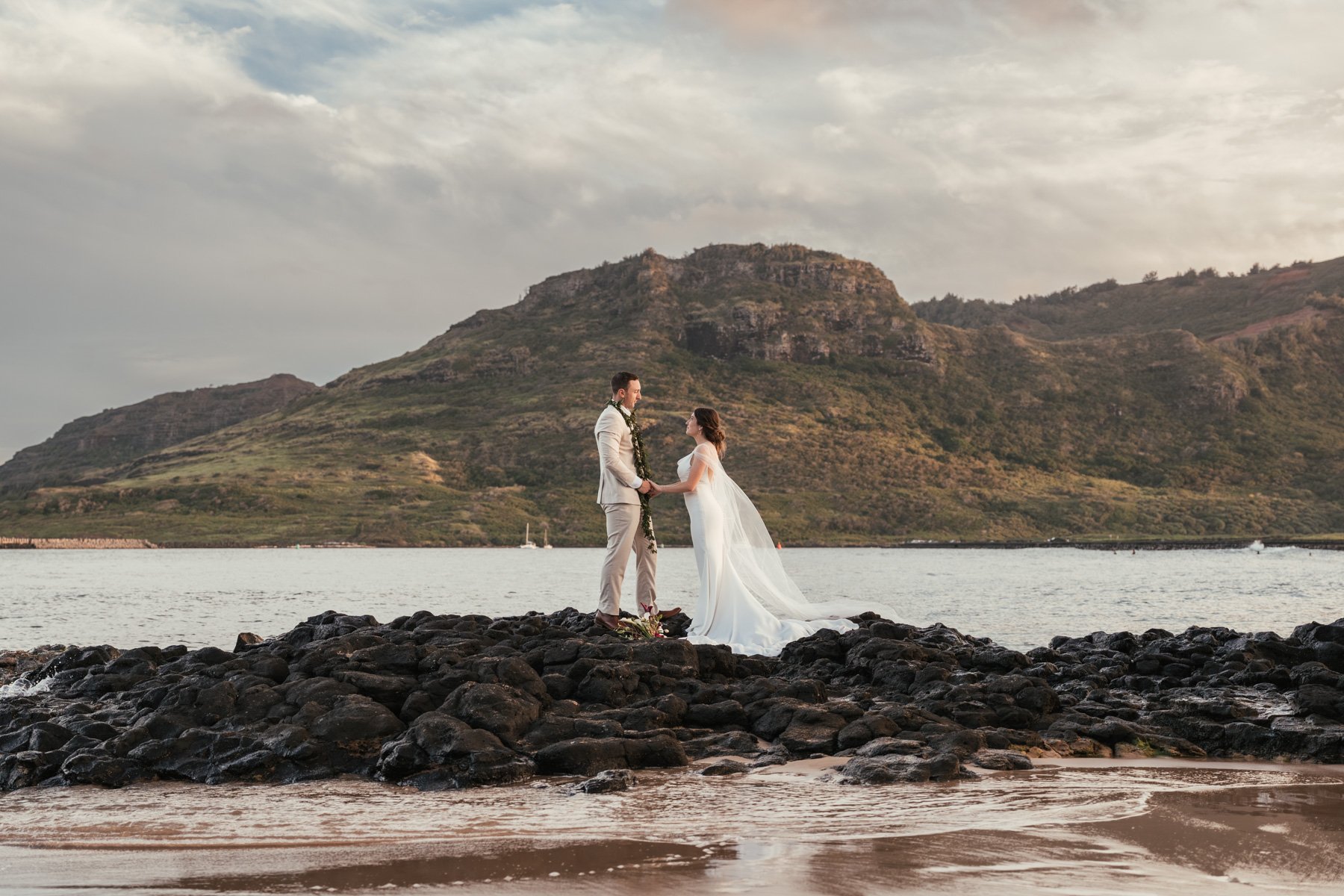 Bride and groom holding hands on lava rocks at sunset on Kalapaki Beach, a short walk from the Royal Sonesta Kauai Resort in Lihue