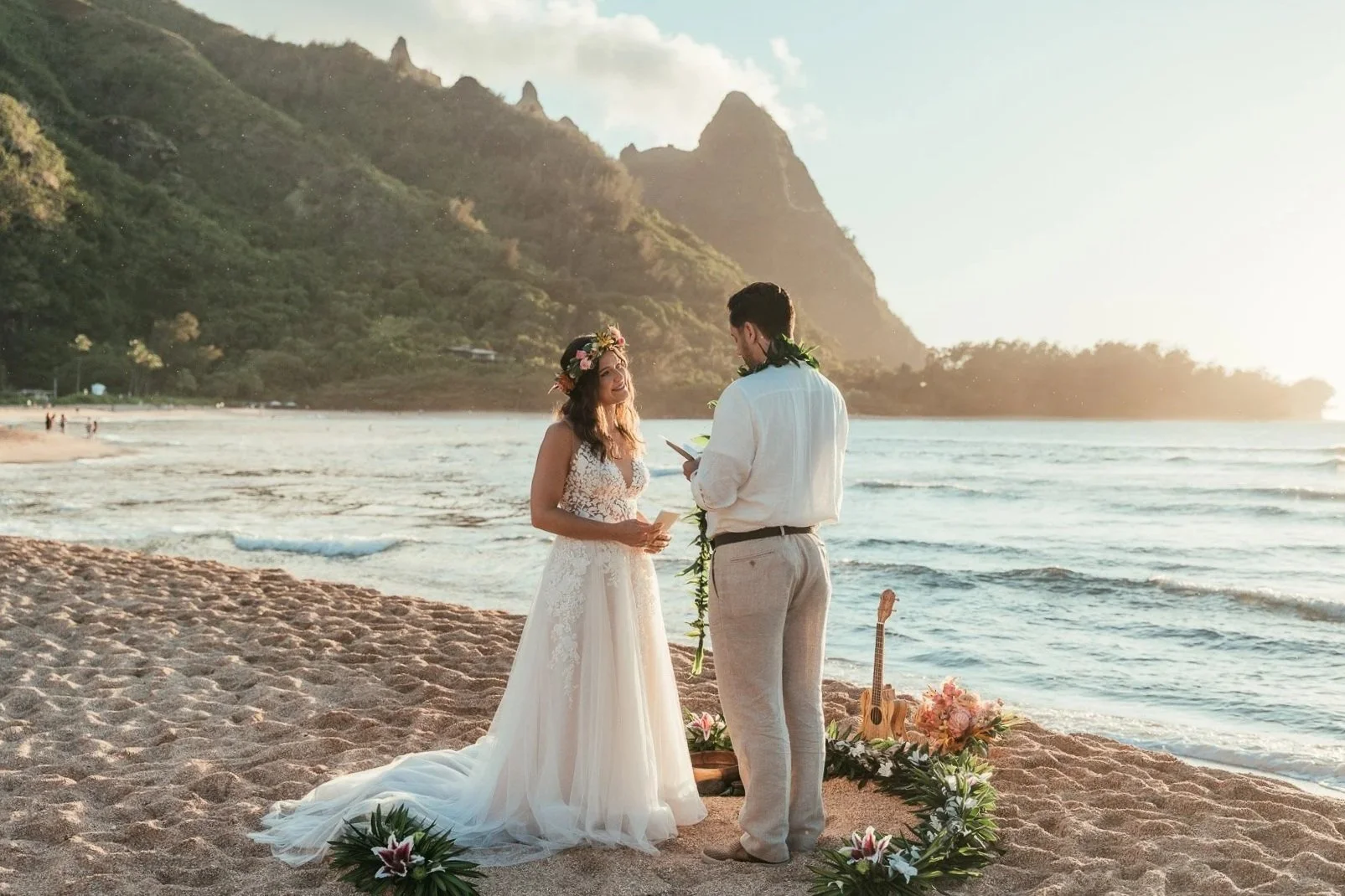 Bride and groom standing on Haena Beach on Kauai with green mountains behind them and a small floral setup in the sand