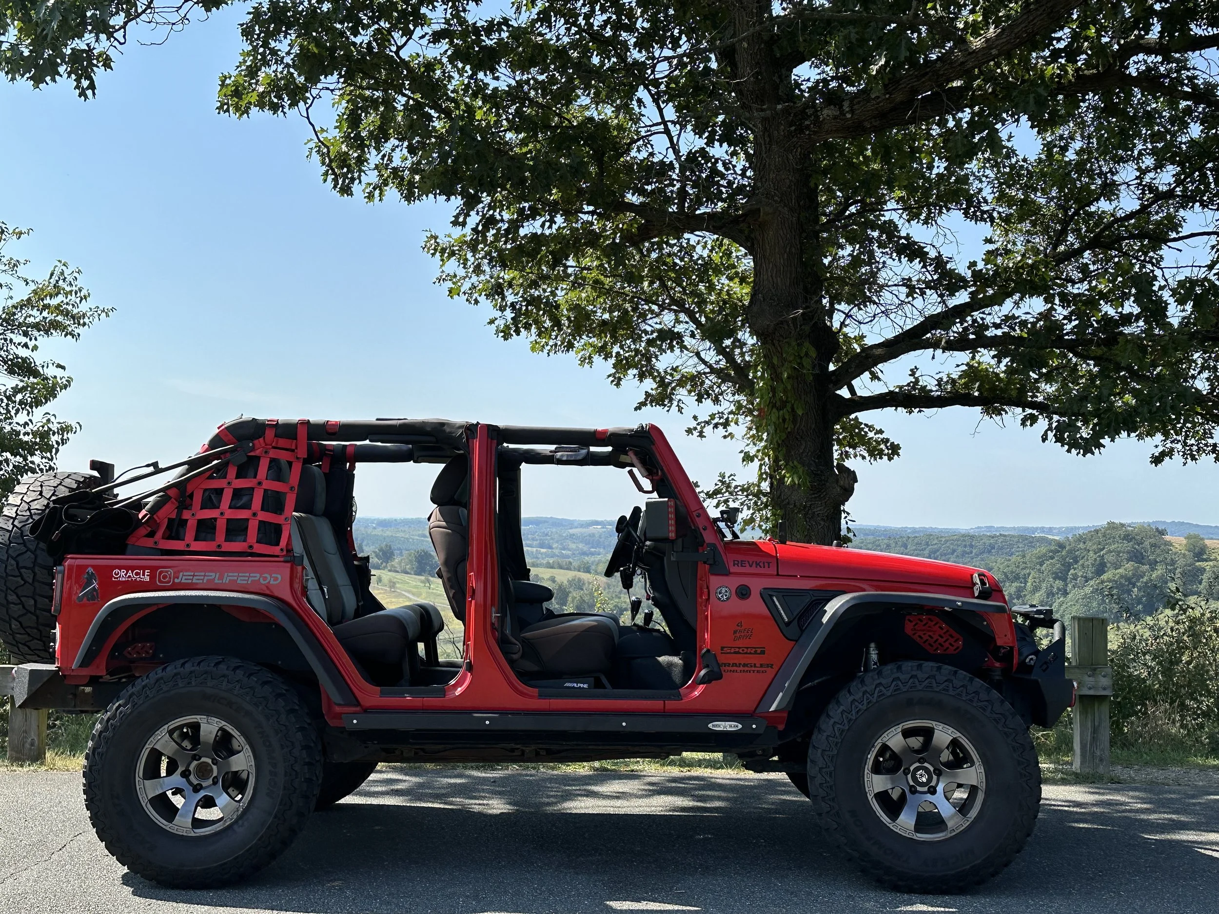 A well built fire-cracker red jeep at mountain overlook with doors off and top down.