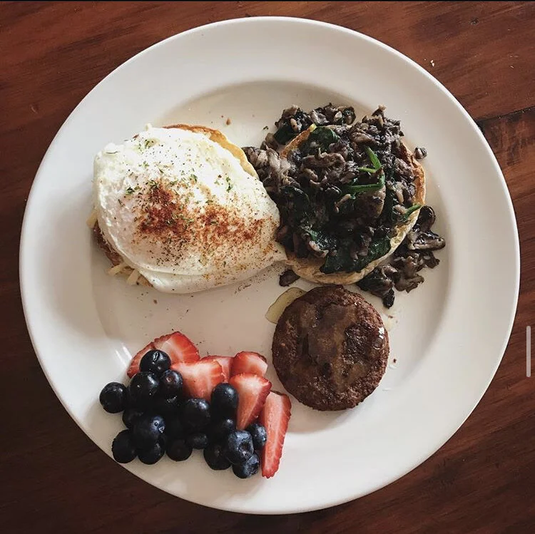 Sourdough English Muffin, fried egg, spinach, mushrooms, and vegan mozzarella, paired with a vegetarian chicken sausage patty w/honey & fresh fruit