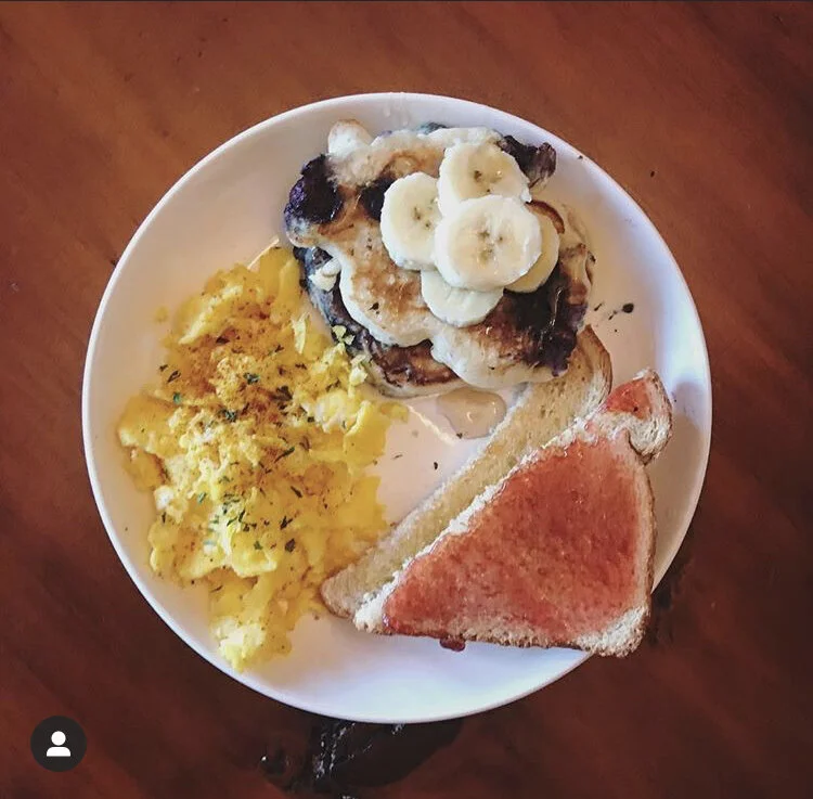 Scrambled eggs seasoned with parsley & paprika, blueberry pancakes topped with bananas & 2 pieces of toast; 1 with strawberry jam & the other honey spread