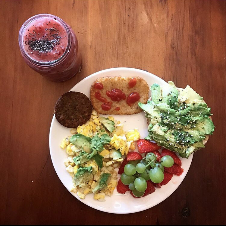 Bagel with Avocado, Scrambled eggs, vegan sausage patty, hash brown, strawberries with grapes, and a Pineapple-cherry smoothie with chia seeds