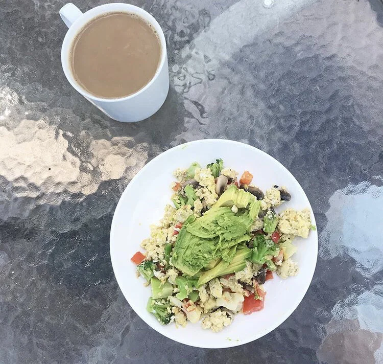 Scramble - egg, tomatoes, broccoli, mushrooms, and avocado, with a cup of coffee 