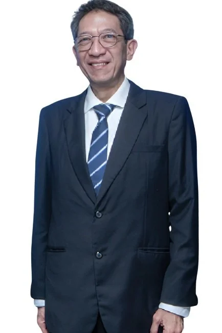 A middle-aged man in a dark blue suit, white shirt, and striped blue tie standing and smiling against a white background.