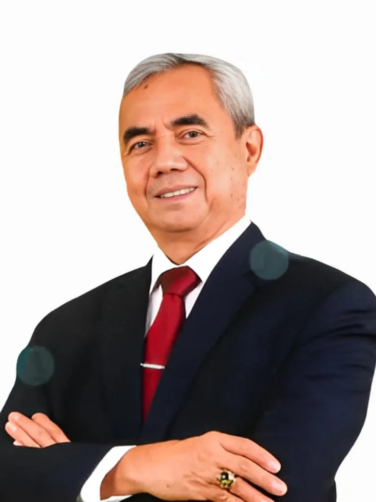 A professional man with gray hair and a friendly smile, wearing a dark suit, white shirt, and red tie, standing with arms crossed against a plain white background.