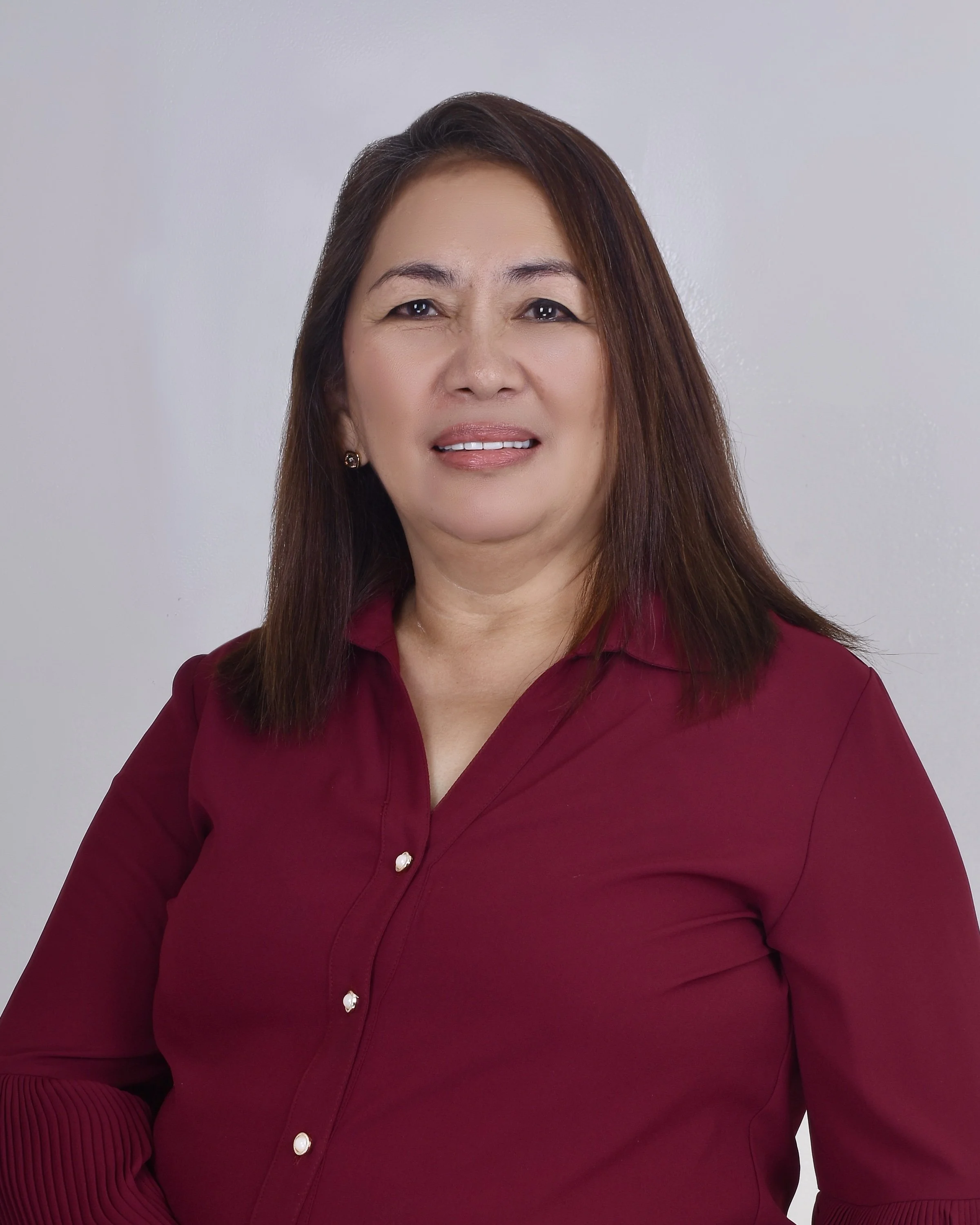 Portrait of a middle-aged woman with straight, shoulder-length brown hair, wearing a burgundy blouse against a plain grey background.