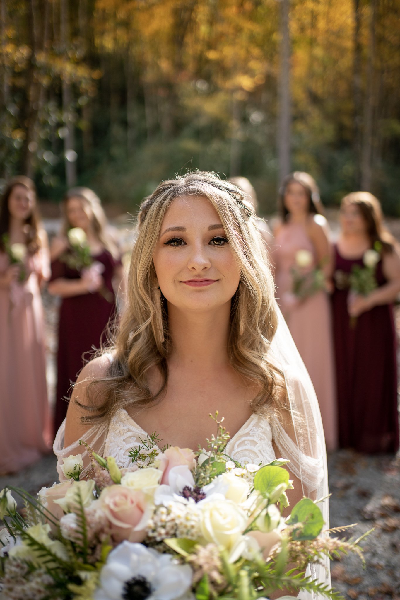 A bride holding a bouquet of flowers, with a group of bridesmaids standing behind her in an outdoor setting with autumn foliage.