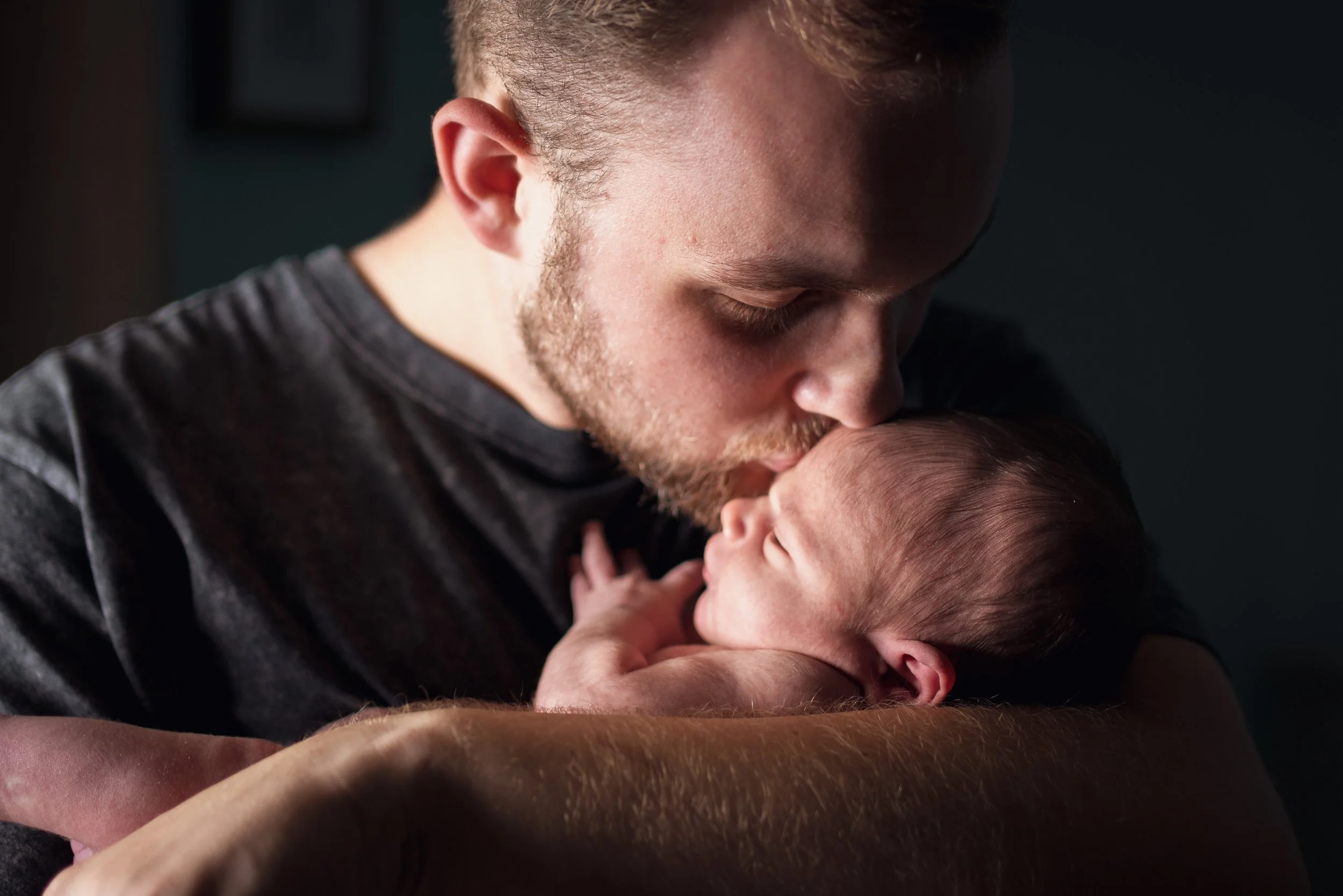 A man holding and gently kissing a newborn baby.