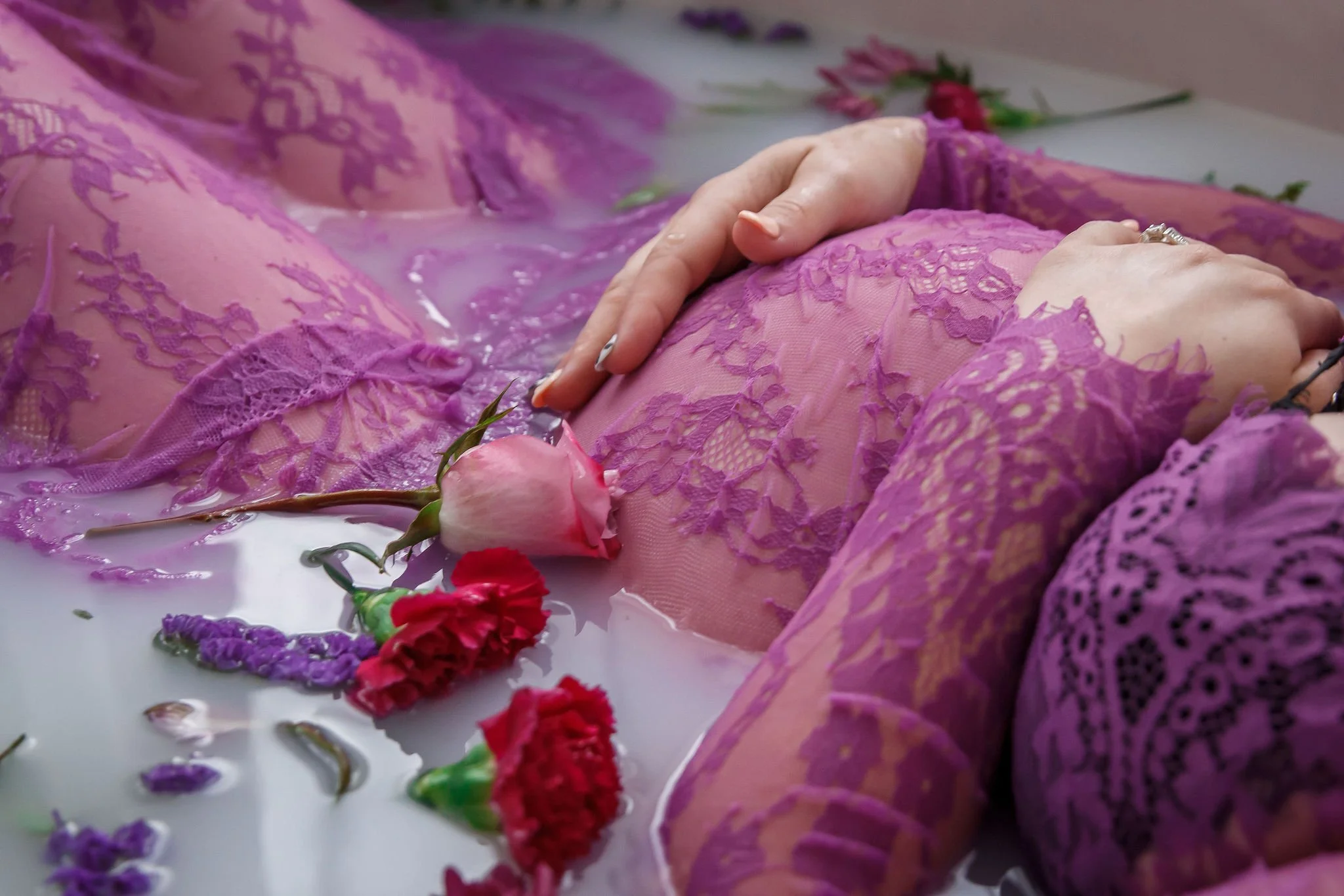 Woman in pink lace dress lying in a milk bath with pink and purple flowers floating around her.