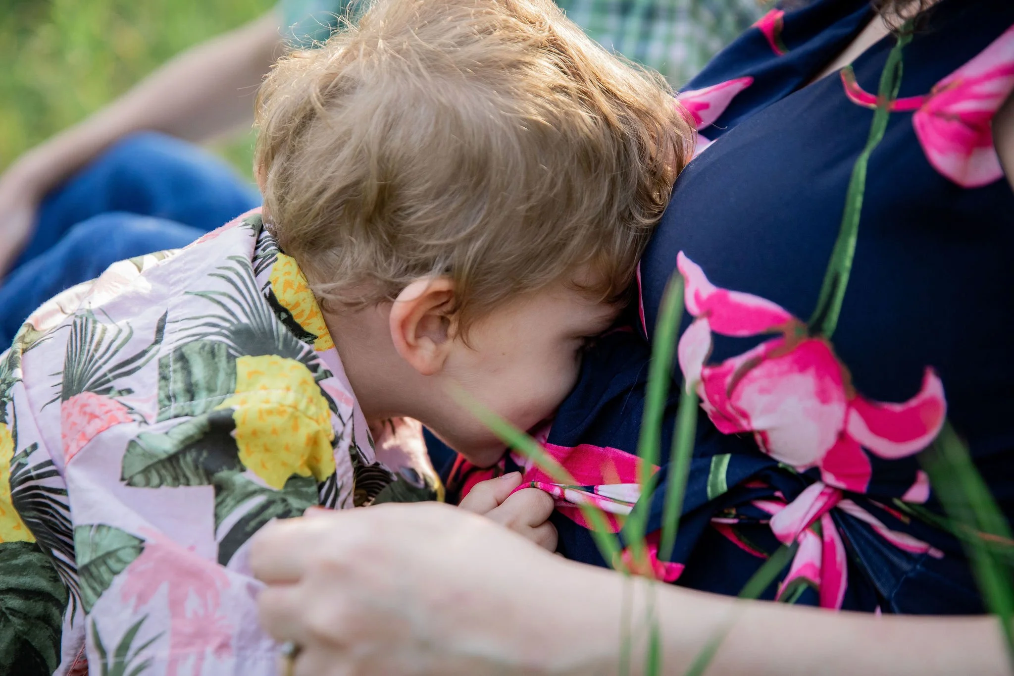 A young boy and a woman are lying on the grass, with the boy resting his head on the woman's chest, in an outdoor setting. maternity family photography at Bow Valley Habitat Station in Calgary Alberta