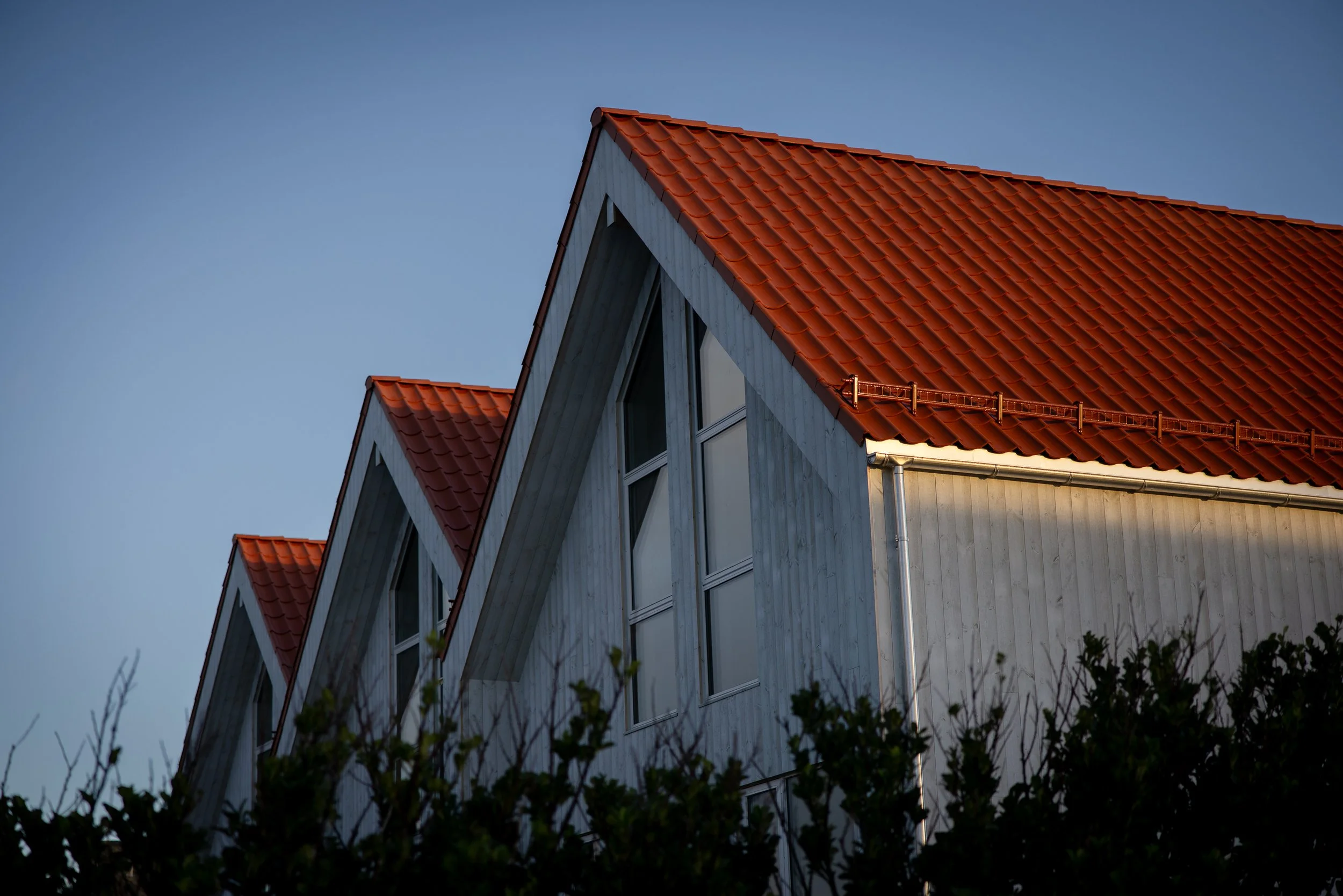 Foto av tre rekkehus på Risøy med hvite vegger og røde takflater sett mot en blå himmel.