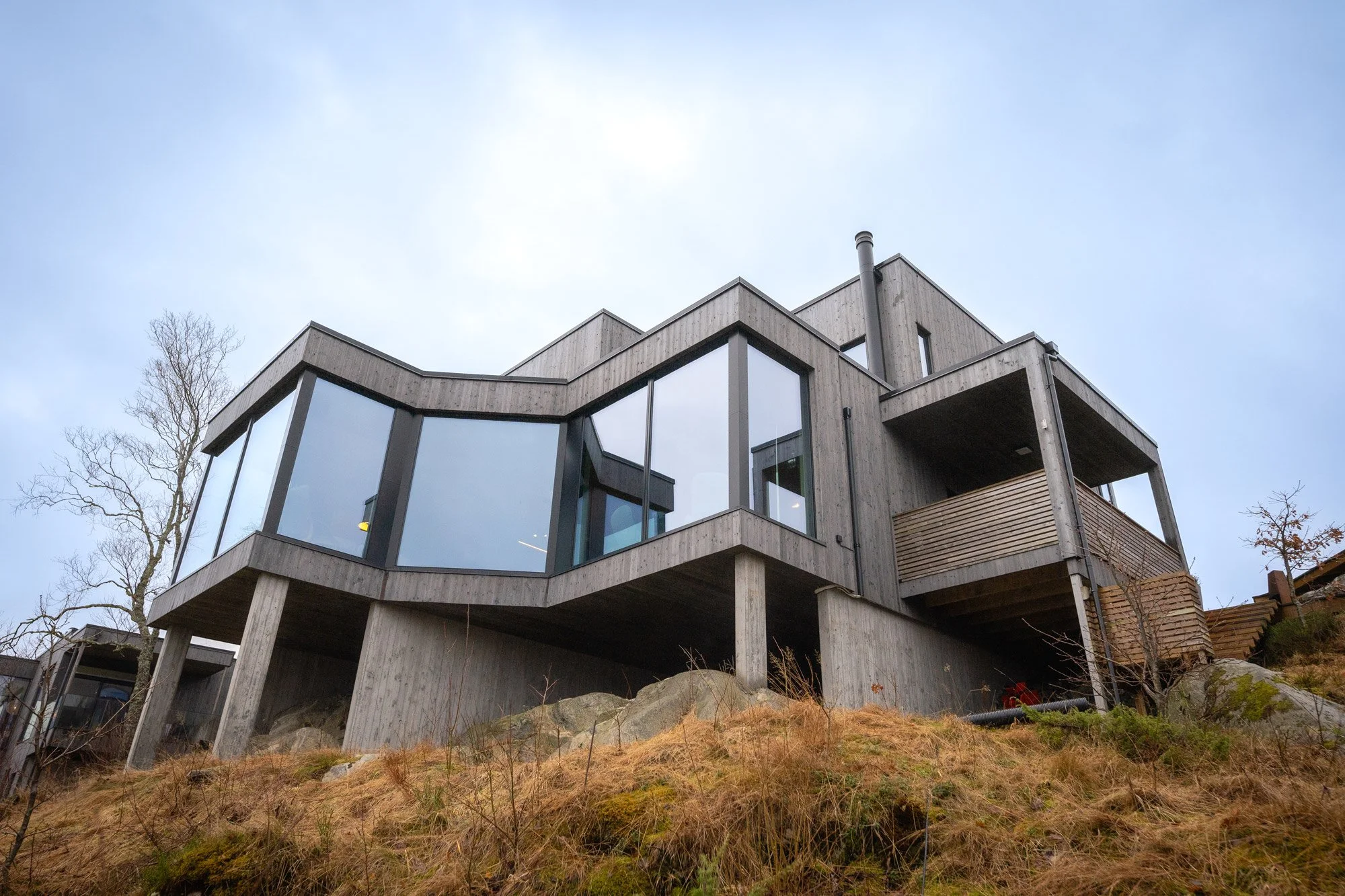 Moderne trehus med store vinduer i skråning, tilpasset terrenget og naturen.