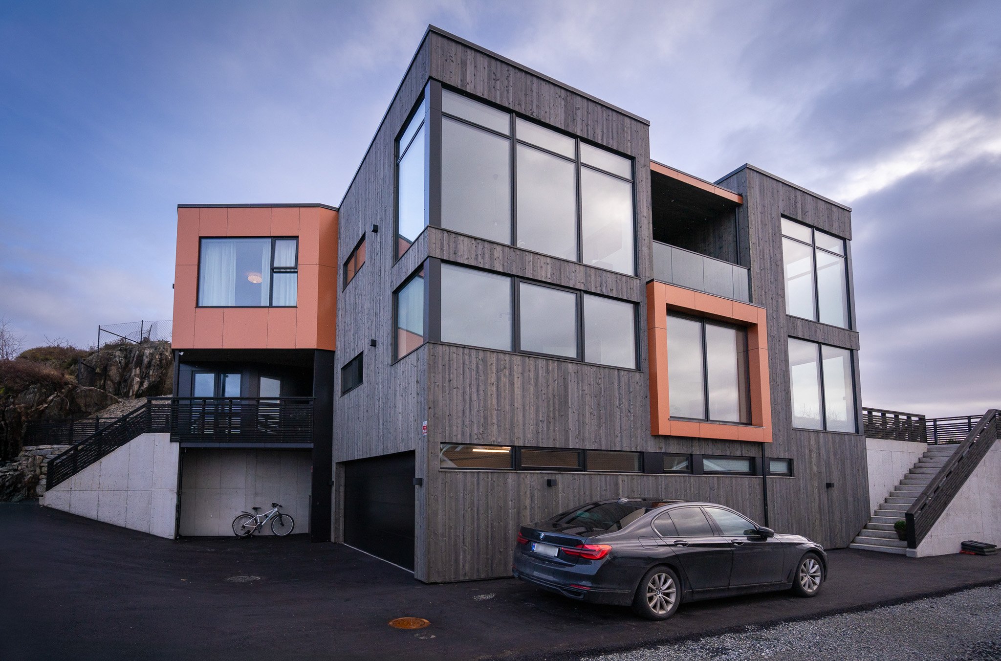 Moderne boligbygning i Haugesund med store vinduer og en sort bil parkert foran, i et oppsett med trapper og eksterne terrasser. Bygget av Byggdetalj.