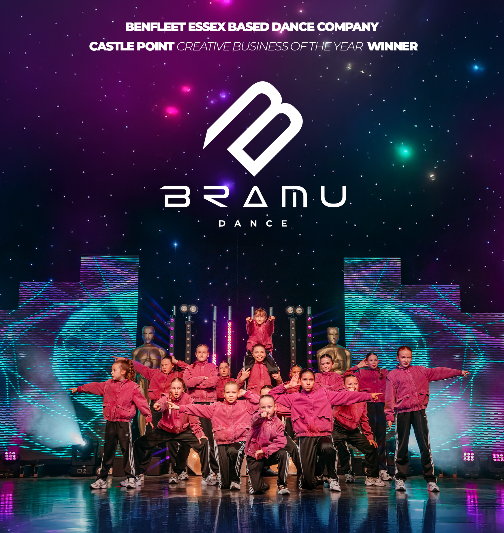 A group of young dancers performing on stage in matching pink jackets, black pants, and white sneakers. The stage features a digital background with colorful lines and shapes, and a large logo reading 'BRANDU DANCE' above them. The backdrop also displays award recognition for Benfleet Essex Based Dance Company at Castle Point.