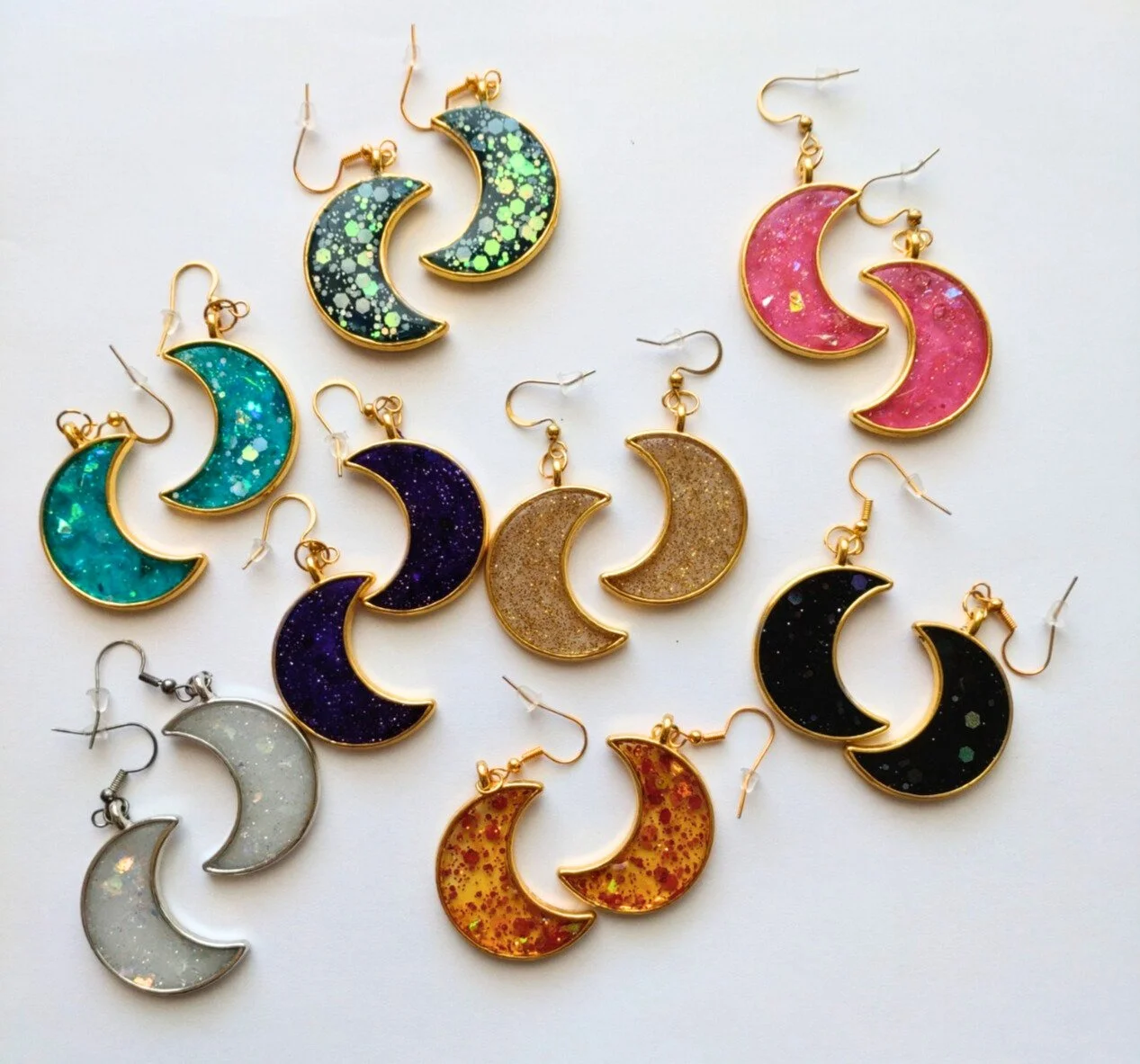 8 pairs of crescent moon earrings in different coloured glittery resin on white background