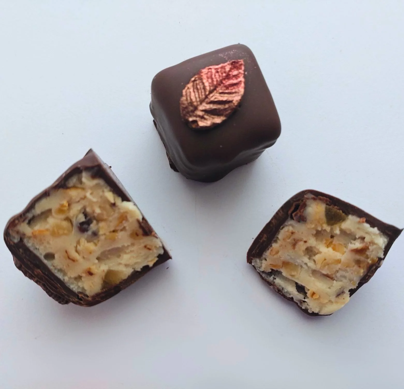 Taste of Autumn dark chocolate with a bronze leaf decoration, alongside two cut halves revealing a white chocolate centre with hazelnuts, crystallised ginger and cocoa nibs.