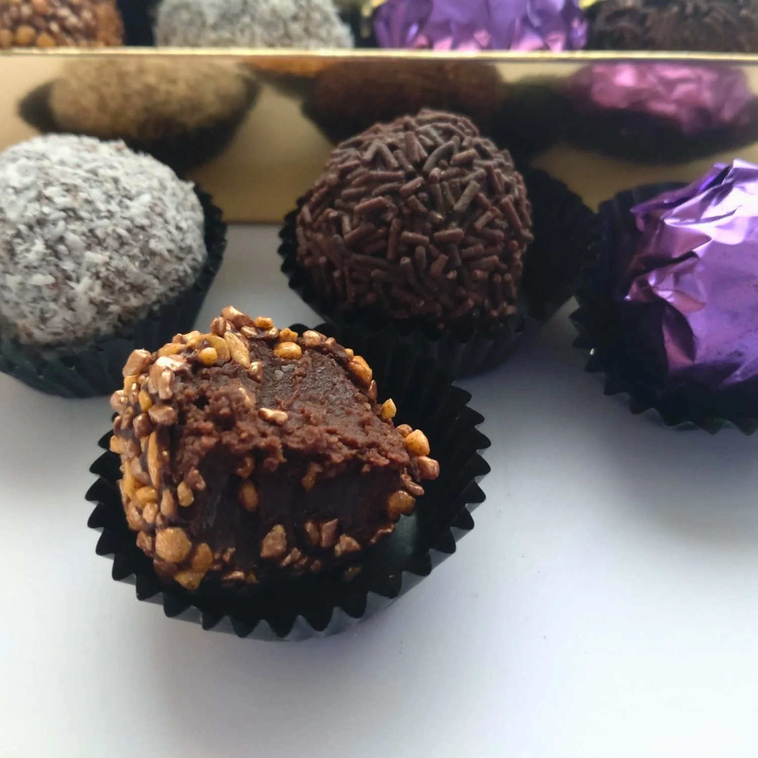 Partially eaten Goddess truffle showing its soft dark chocolate and Cointreau ganache filling, surrounded by a crunchy bronze and gold sugar coating.
