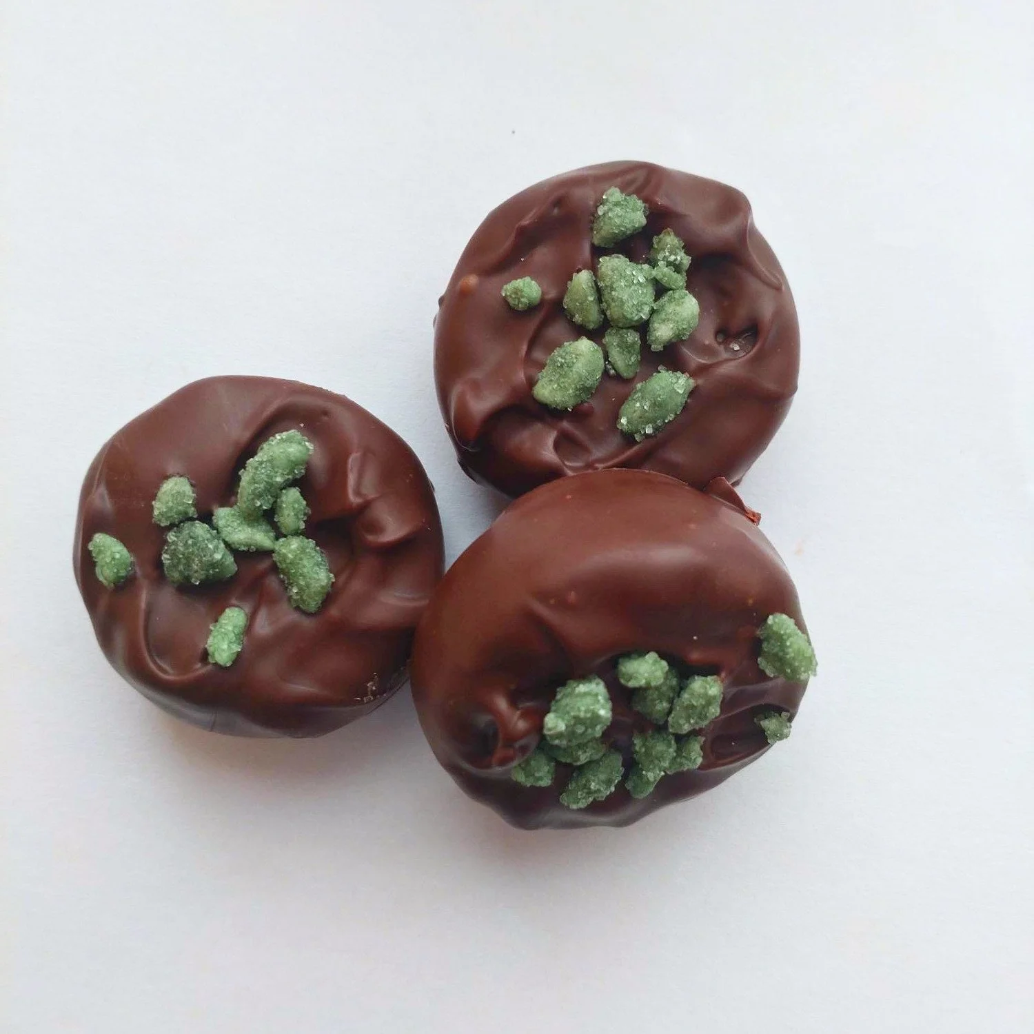 3 dark chocolate peppermint creams on a white background. The chocolates are sprinkled with crystalised mint fragments.