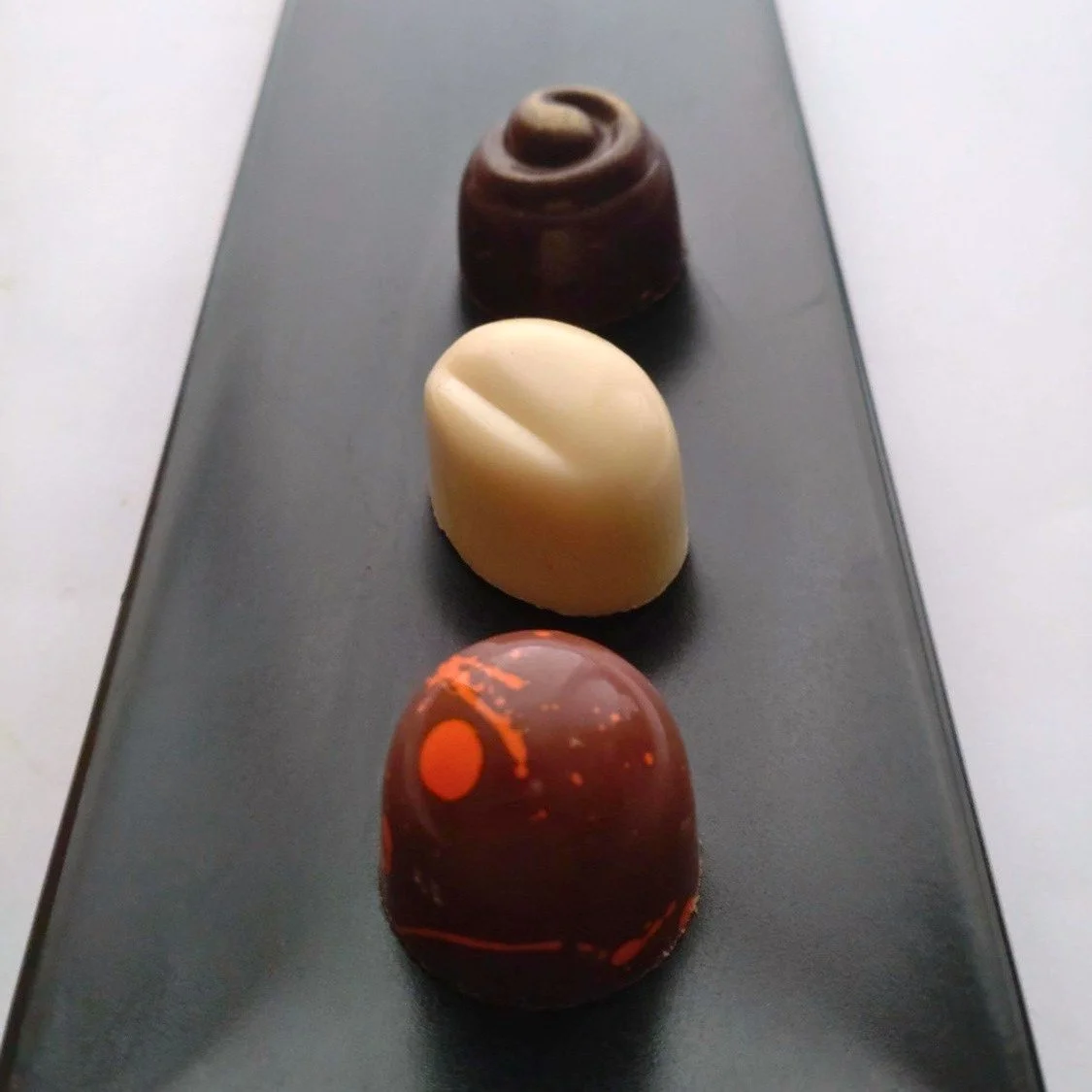 Three Japanese-inspired handmade chocolates arranged on a black serving plate.
