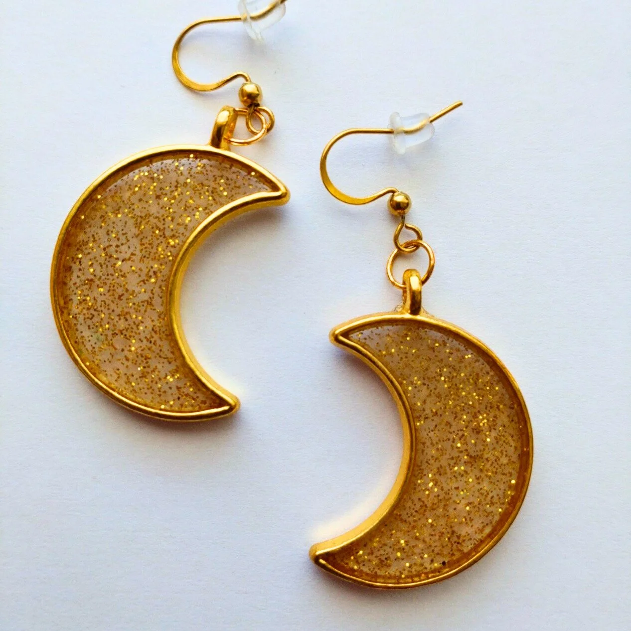 Gold coloured crescent moon earrings in glittery gold resin on white background