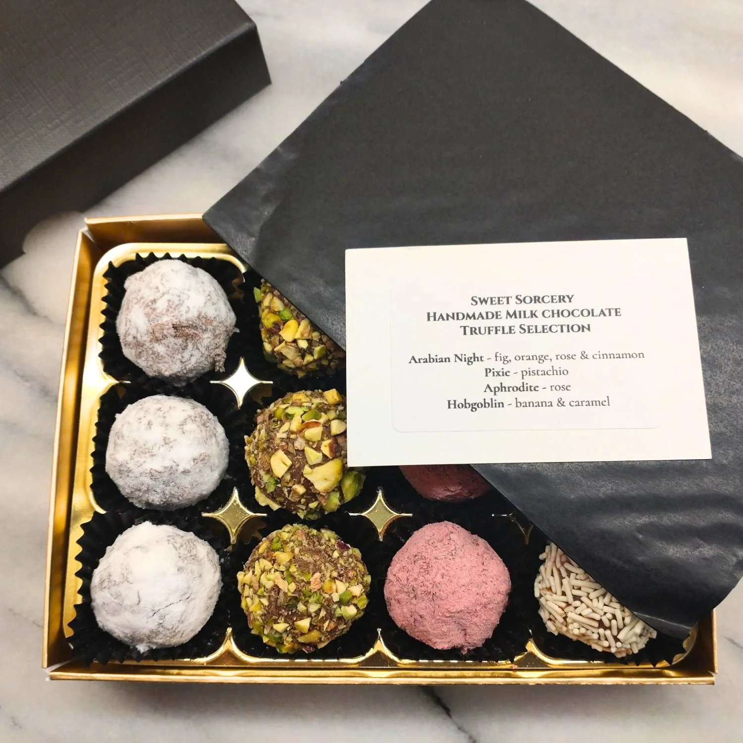 Open box of handmade milk chocolate truffles with a flavour card listing Arabian Night, Pixie, Aphrodite and Hobgoblin.