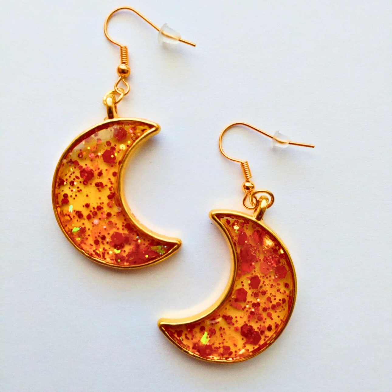 Gold coloured crescent moon earrings in glittery orange resin on white background