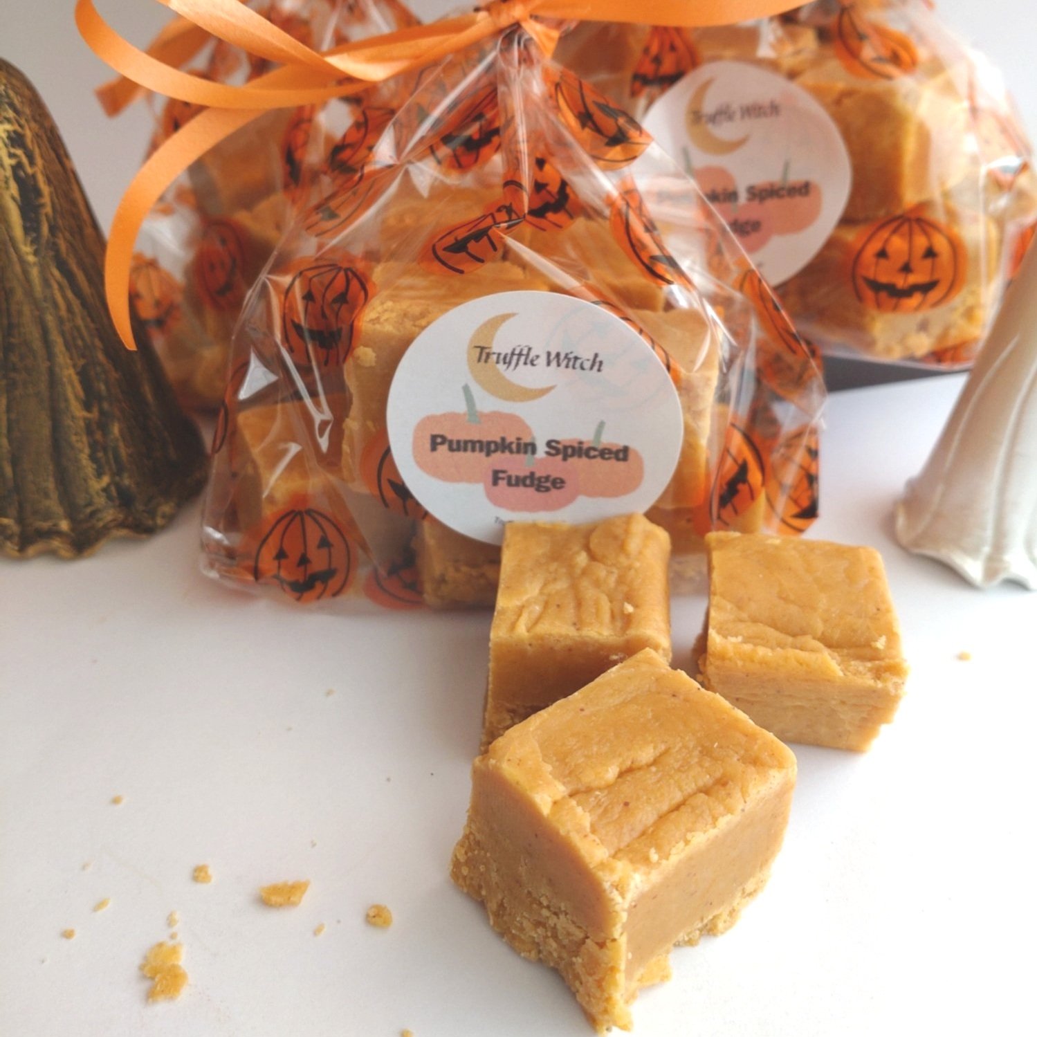 Bags of pumpkin spiced fudge with 3 squares of fudge in front  on a white background