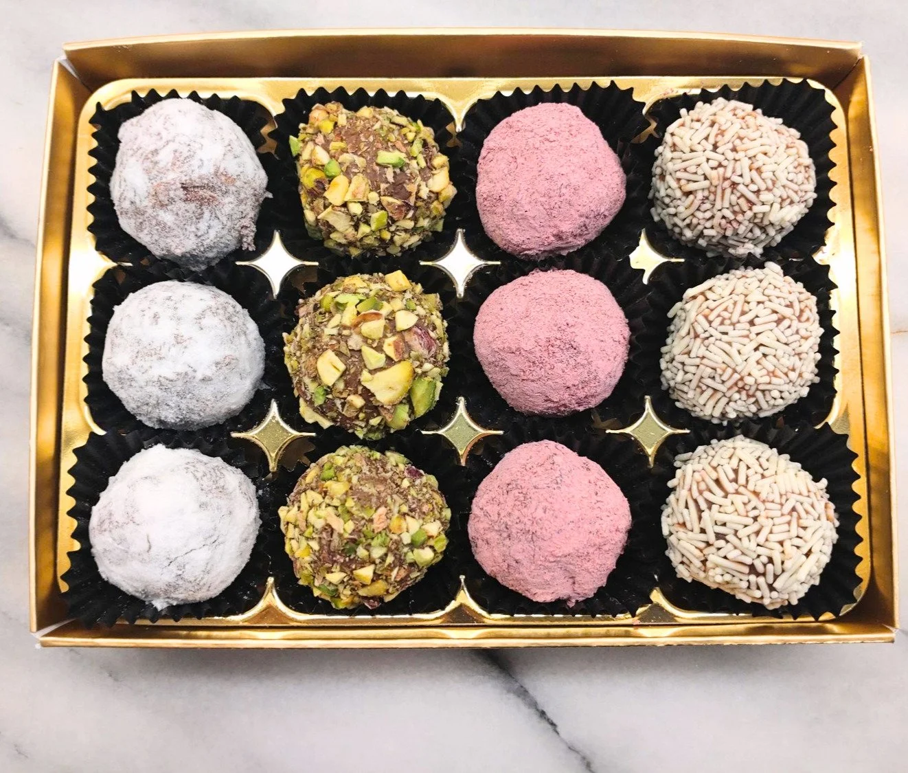 Open gift box containing twelve handmade milk chocolate truffles in four different finishes.
