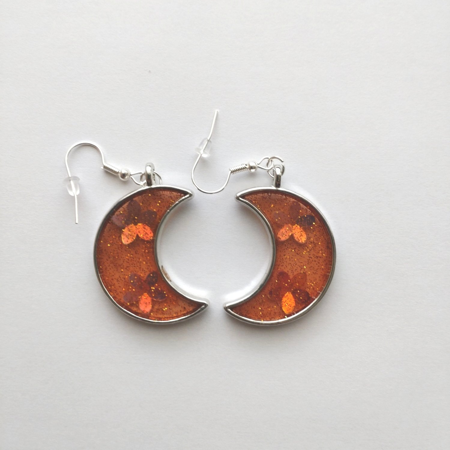 A pair of glittery orange crescent moon earrings on a white background