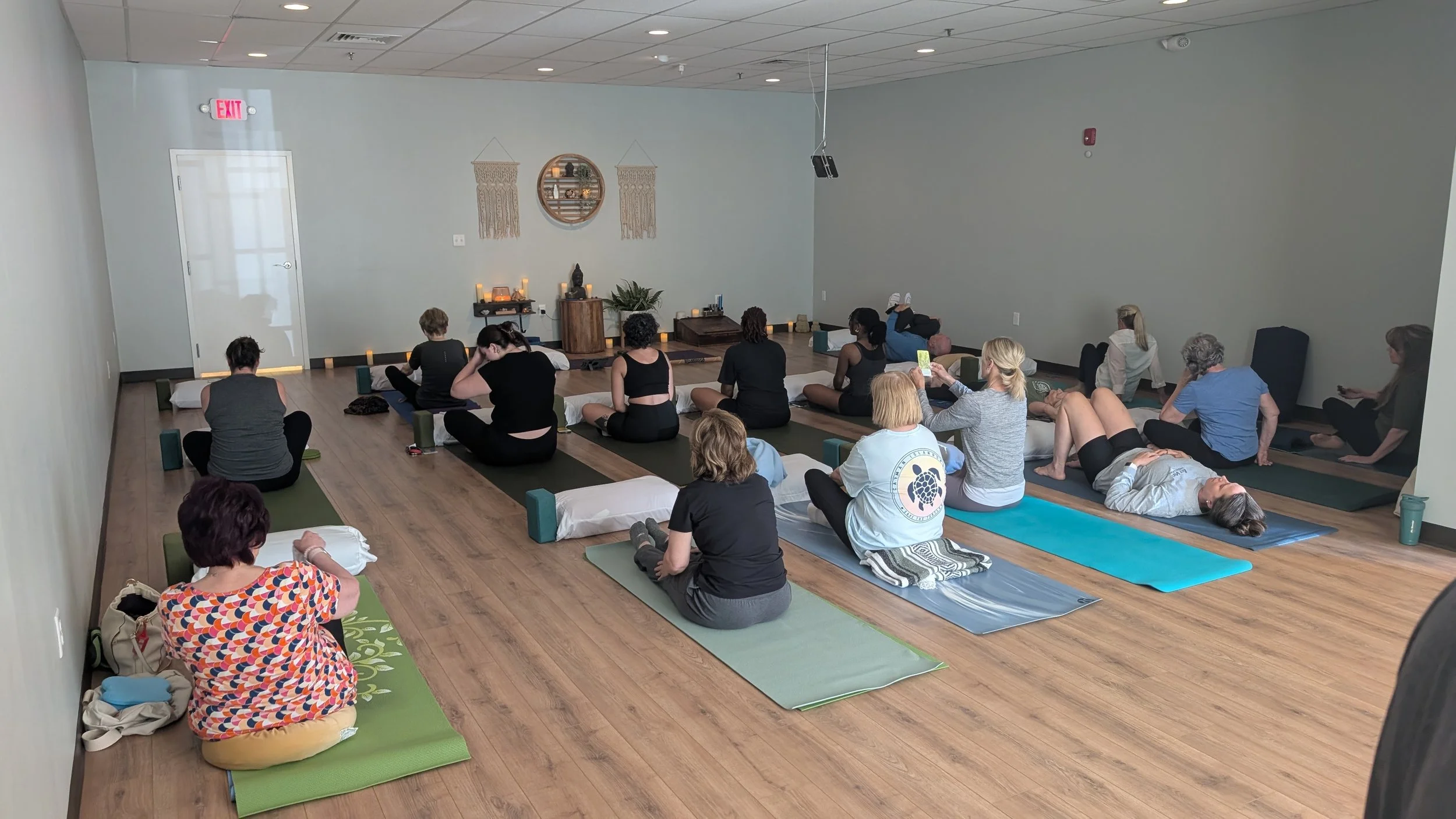 A full yoga class seated on mats in the bright studio at Emerald Yoga Studio in Pembroke, MA, near Marshfield