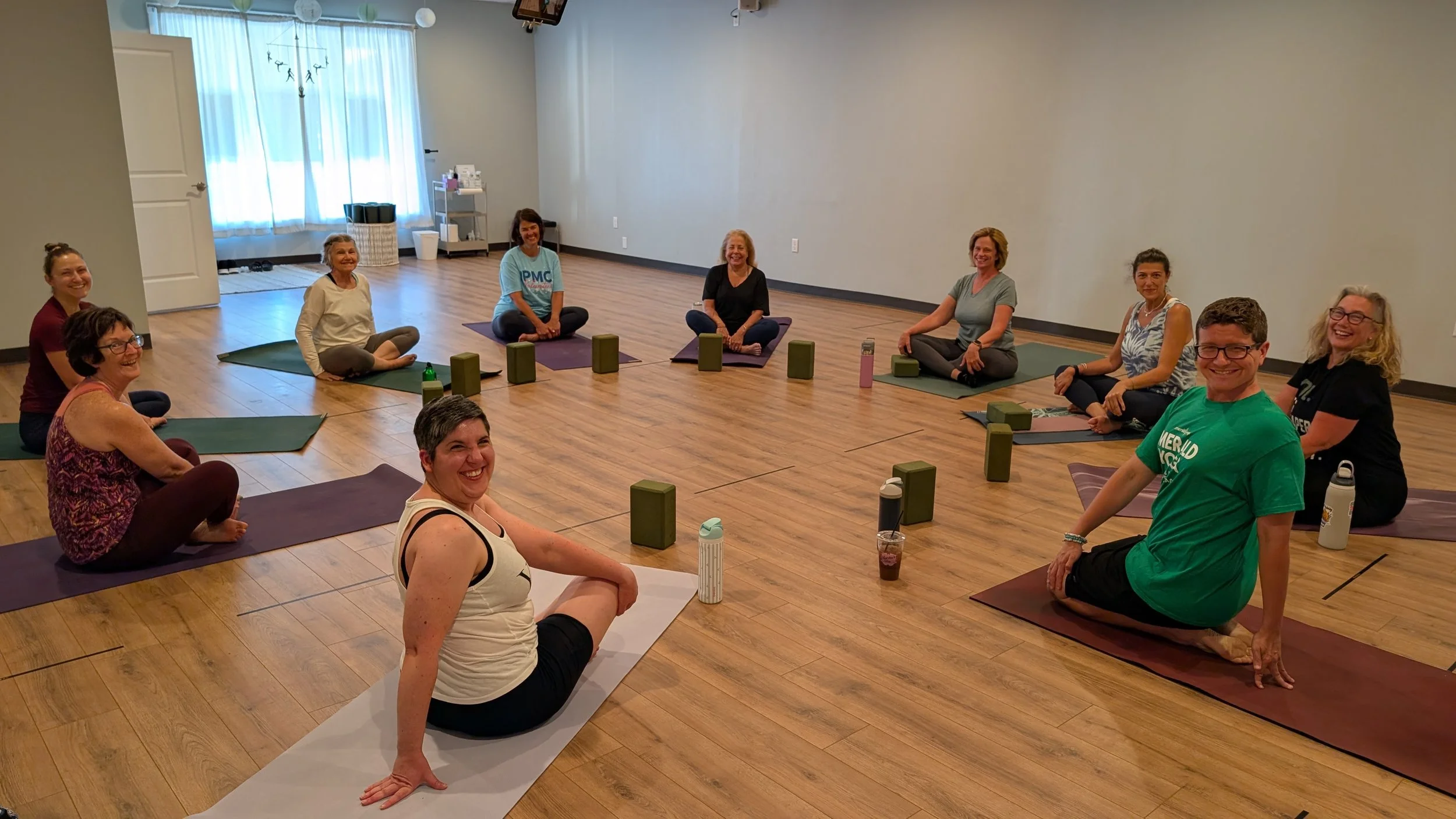 Smiling yoga students seated in a circle on their mats at Emerald Yoga Studio in Pembroke, MA, near Duxbury