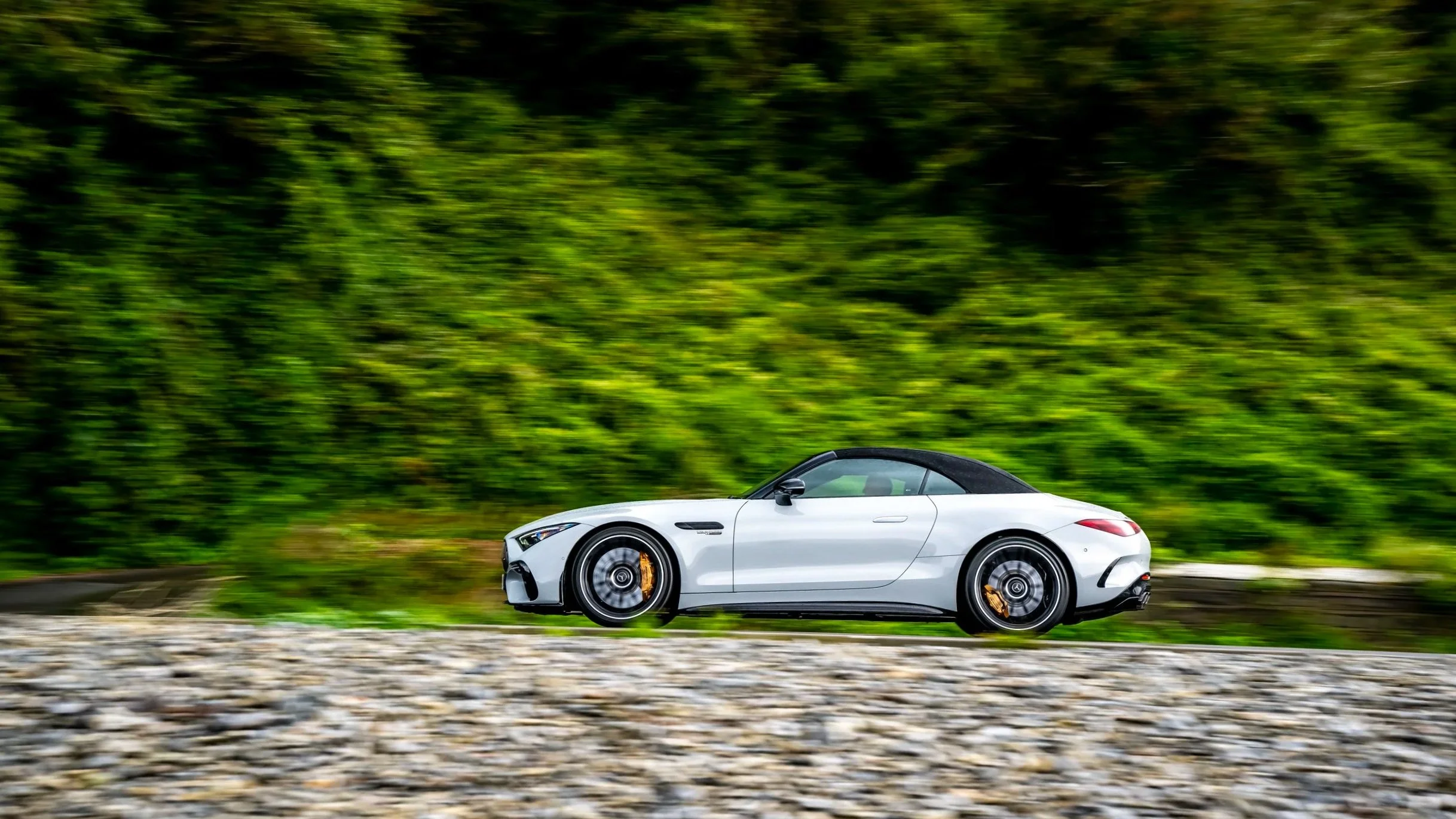 A white convertible sports car driving on a road with green foliage in the background.