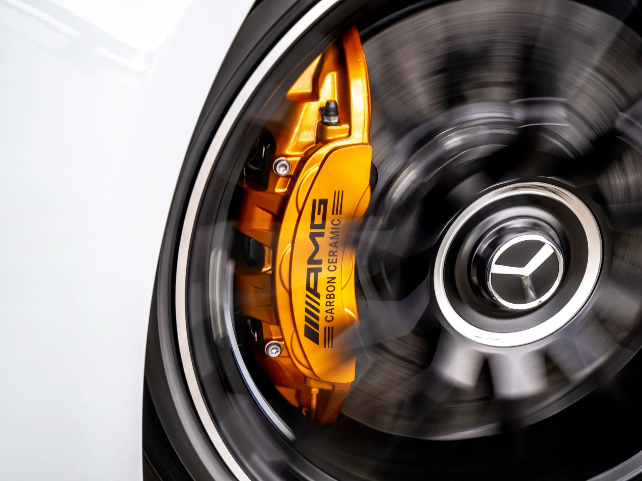Close-up of a car wheel with a spinning black tire, silver rim, and a gold brake caliper marked "Mercedes AMG Carbon Ceramic".