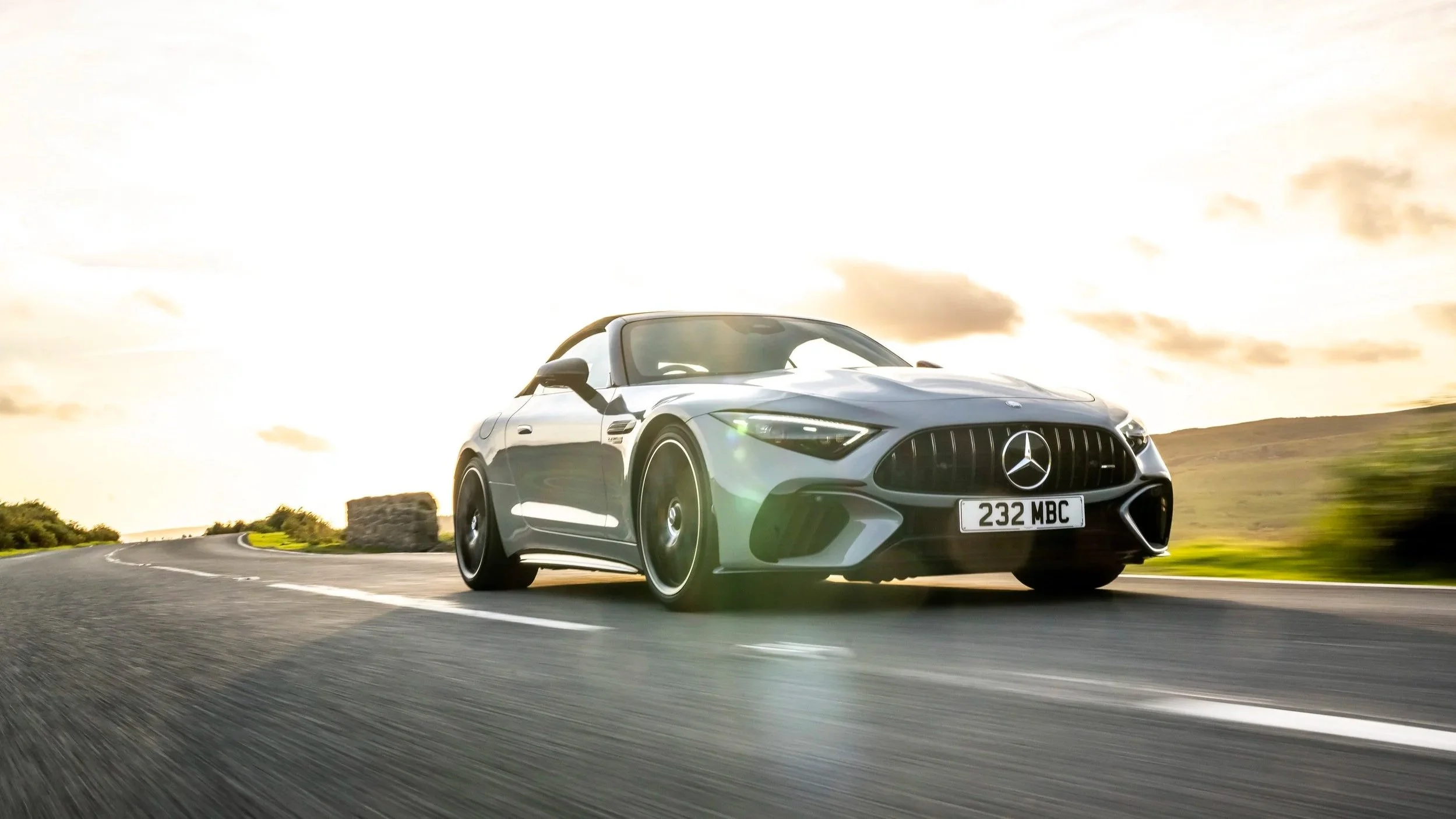 A silver Mercedes-Benz sports car driving on a curving road during sunset.