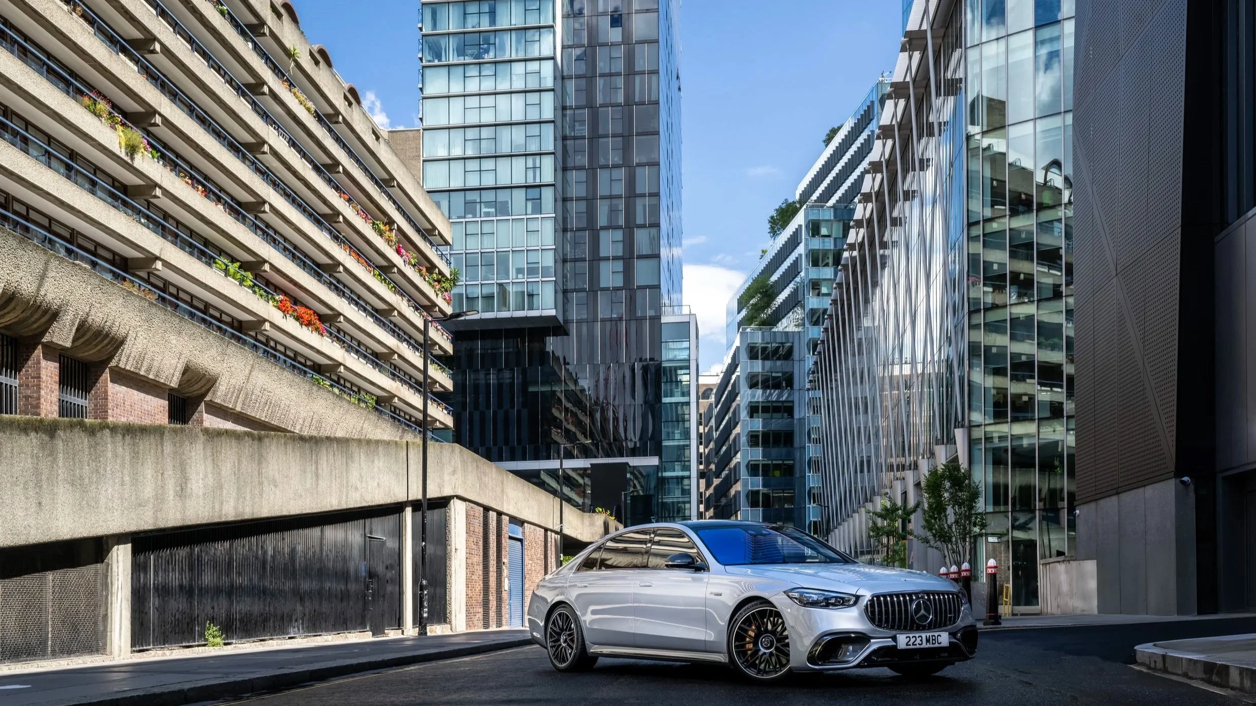 A white Mercedes-Benz car parked on an urban street surrounded by modern glass and concrete high-rise buildings.