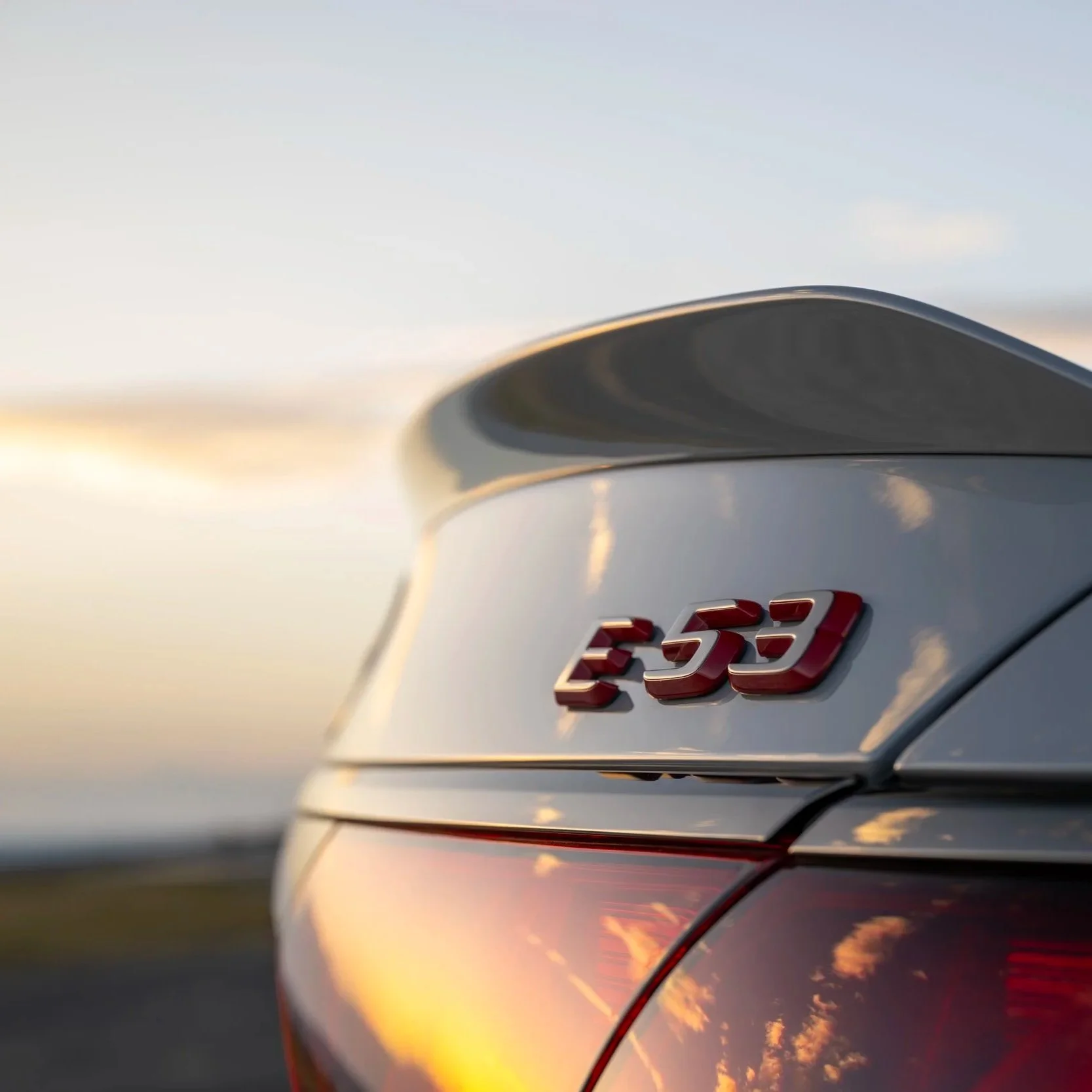Close-up of the rear end of a silver Mercedes-Benz E 53 car with red badge, during sunset.