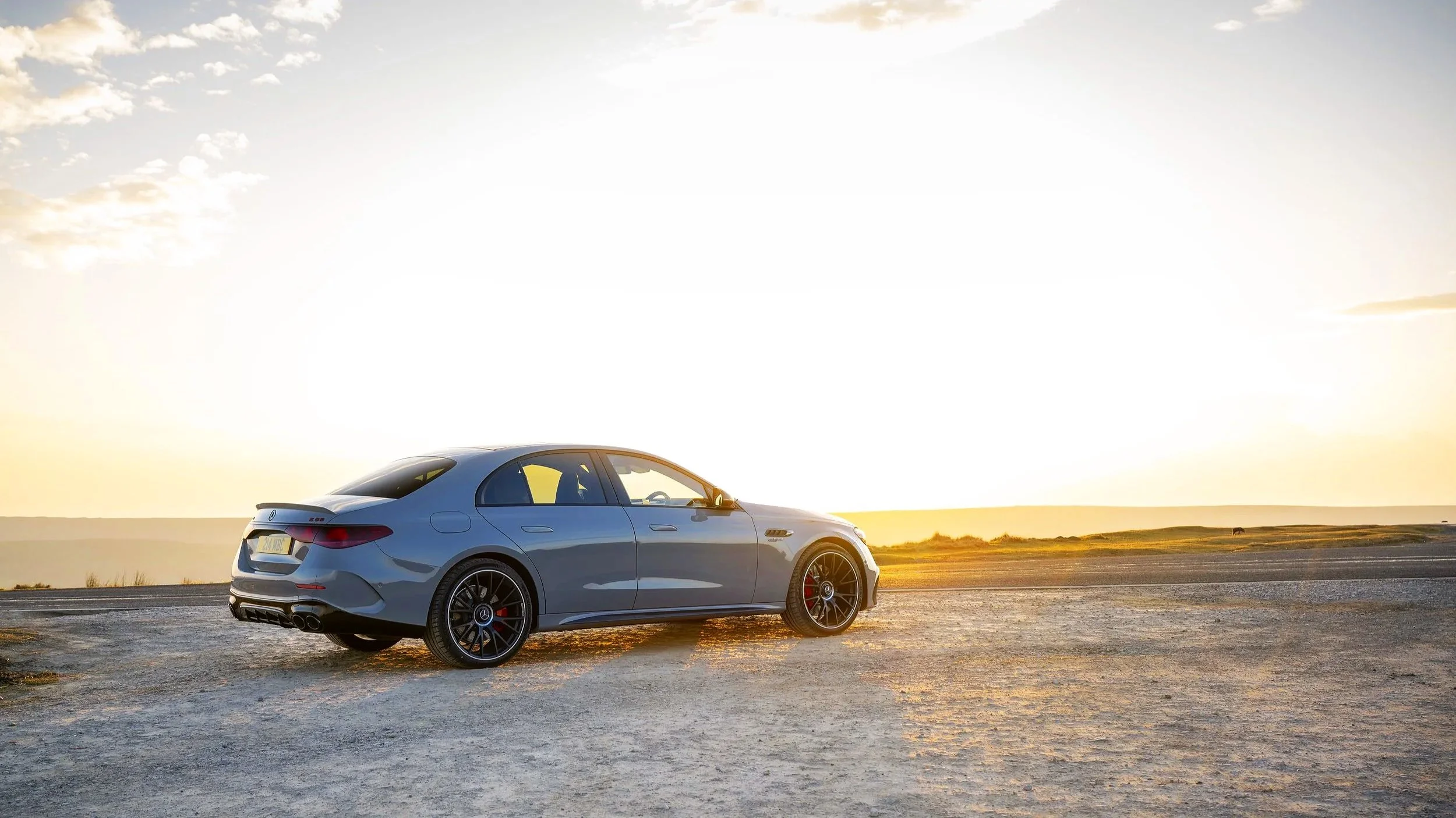 A gray luxury sedan parked on a rough dirt road during sunset with a vast open landscape in the background.