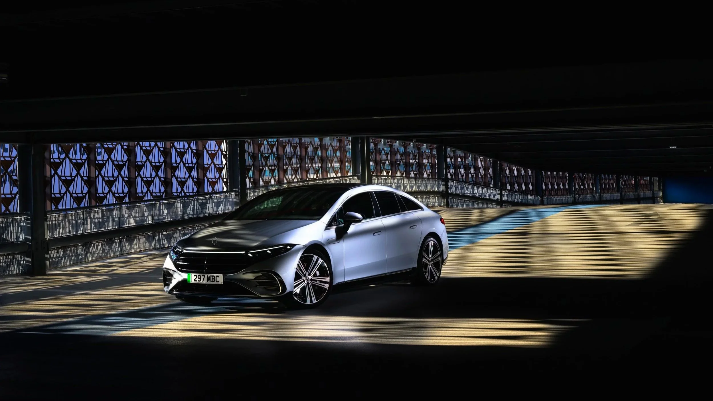 A silver sedan parked in a dimly lit underground parking garage with patterned windows in the background.
