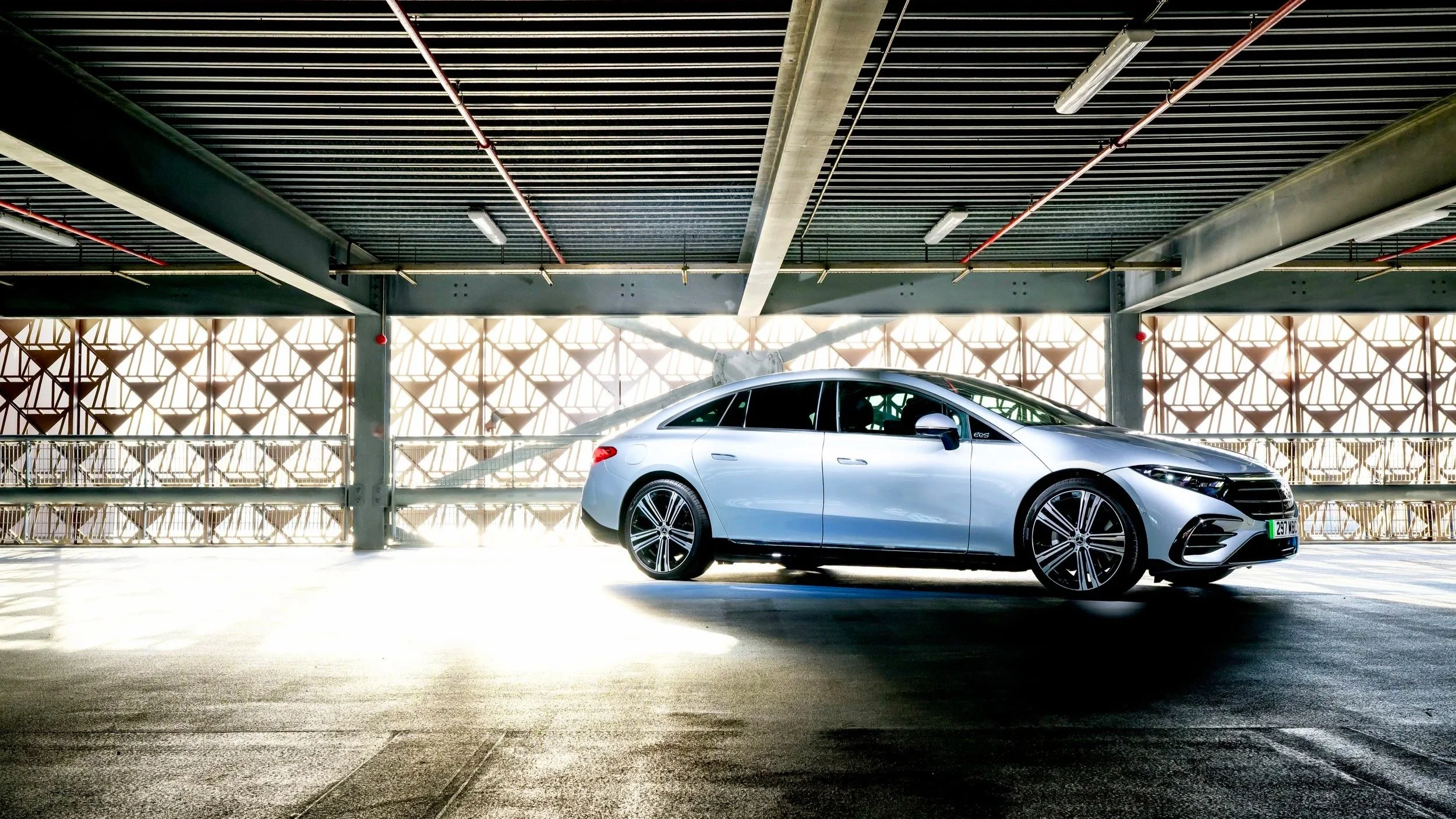 A silver sedan car parked in an indoor parking garage with geometric patterned wall panels and overhead lights.