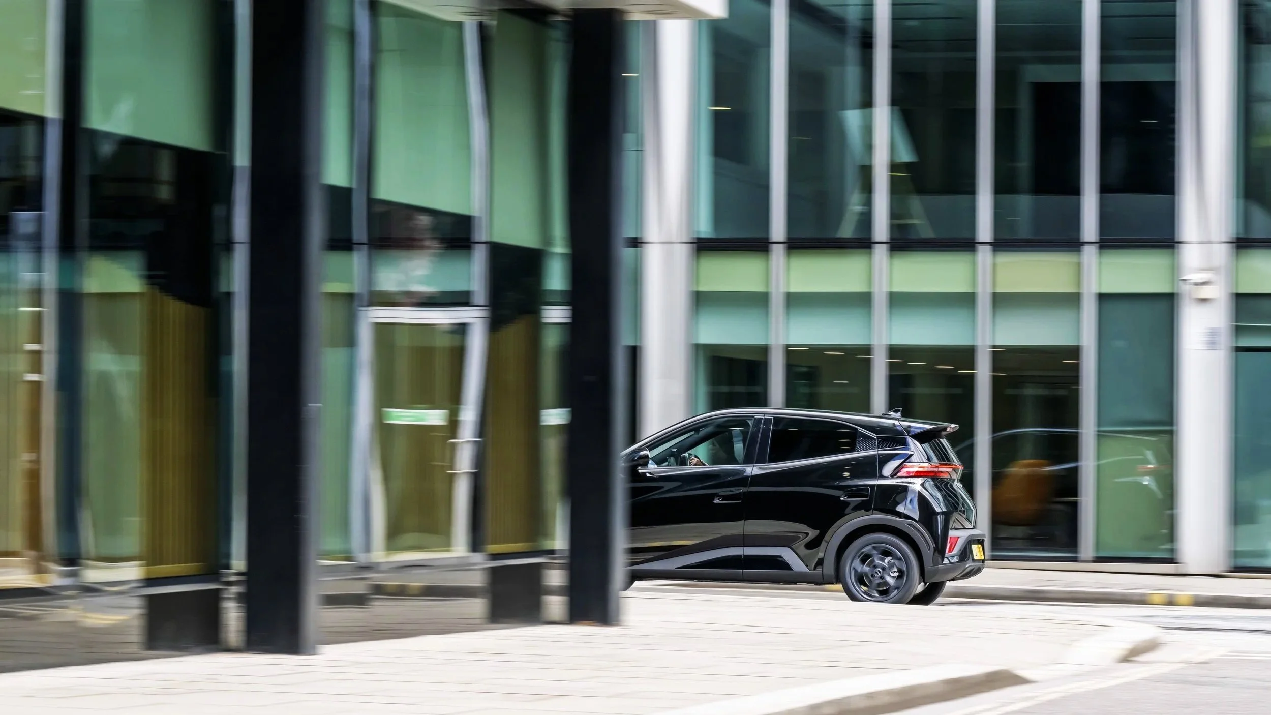 A black compact SUV parked on the city street in front of a modern glass building with green and yellow accents.