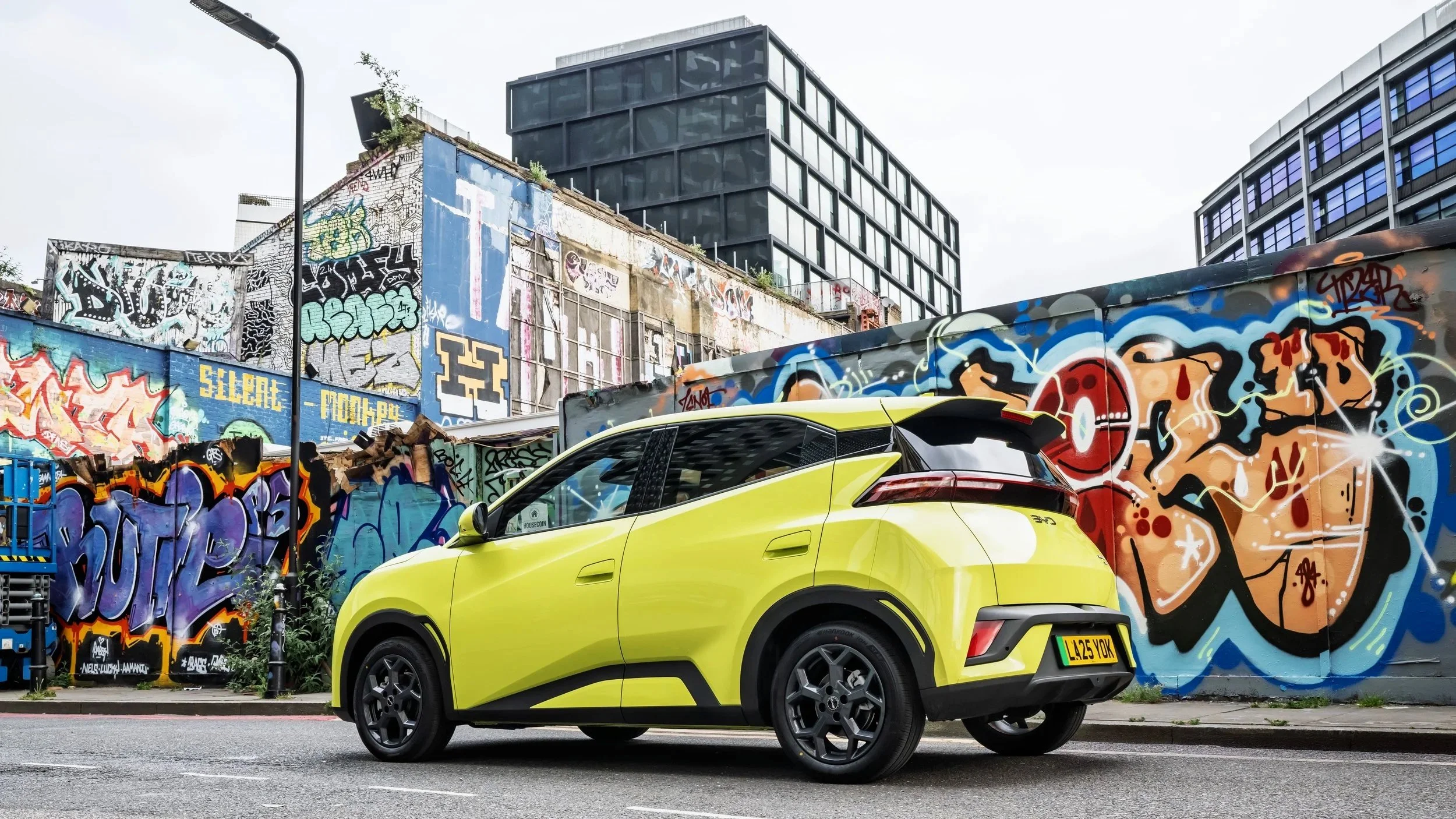 A bright yellow compact SUV parked on the street against a backdrop of colorful graffiti-covered walls and modern black buildings.