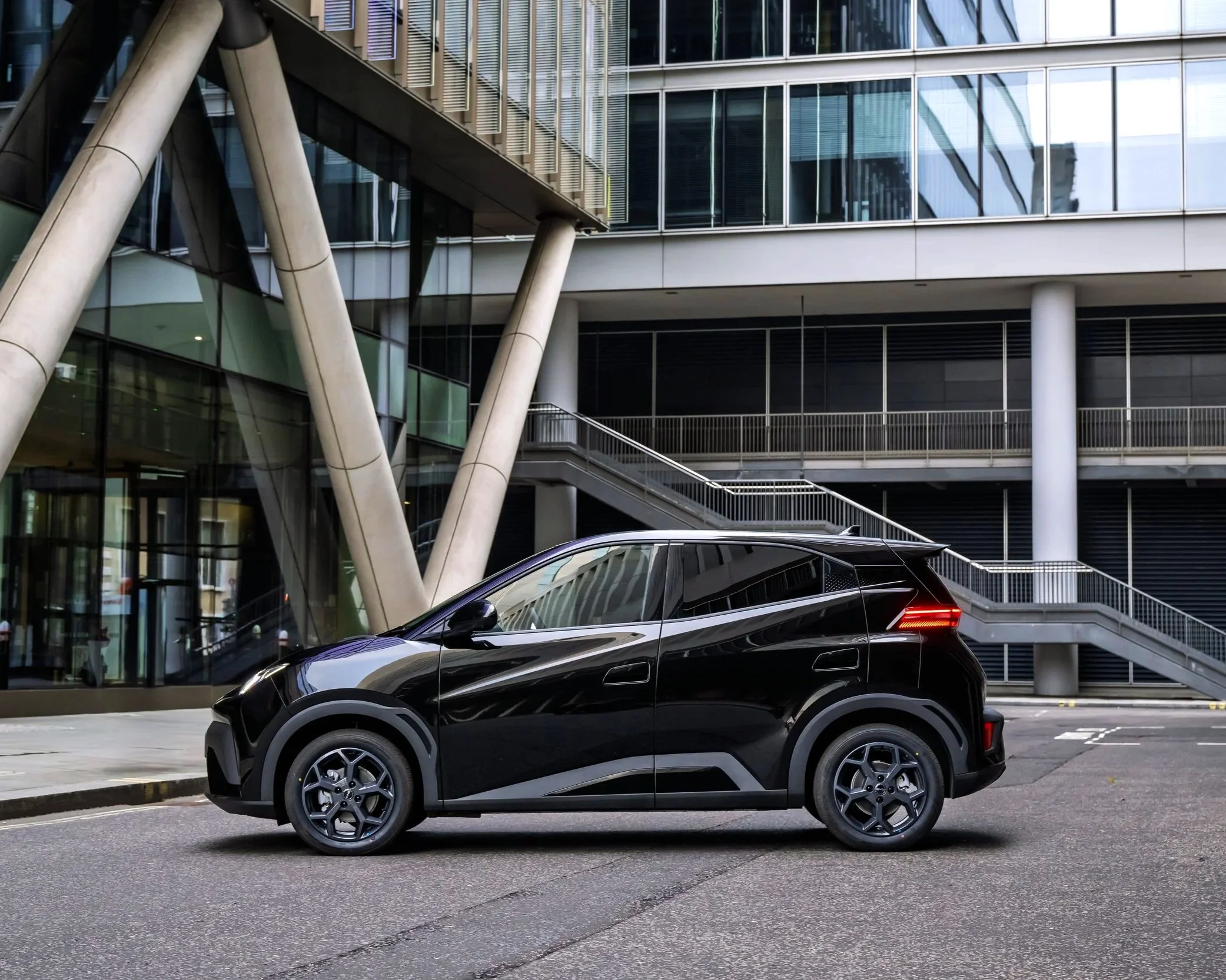 Black compact SUV parked on the street in front of a modern glass building with metal and concrete architectural features.