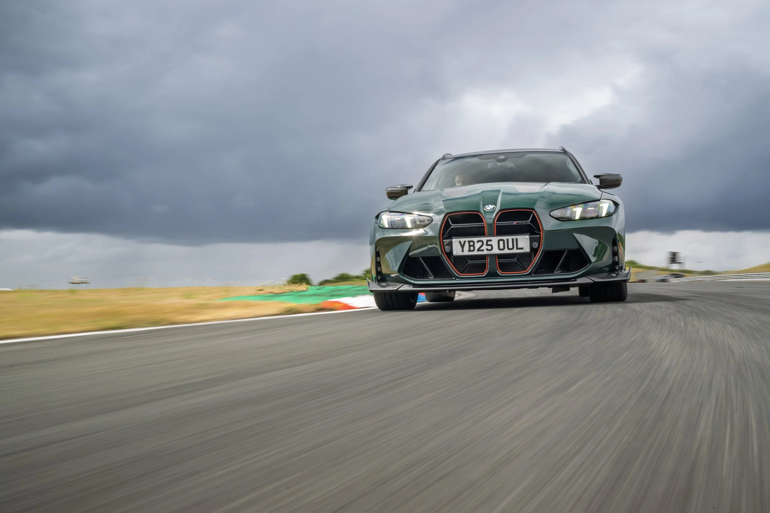 A dark green BMW sports car driving on a race track under a cloudy sky.