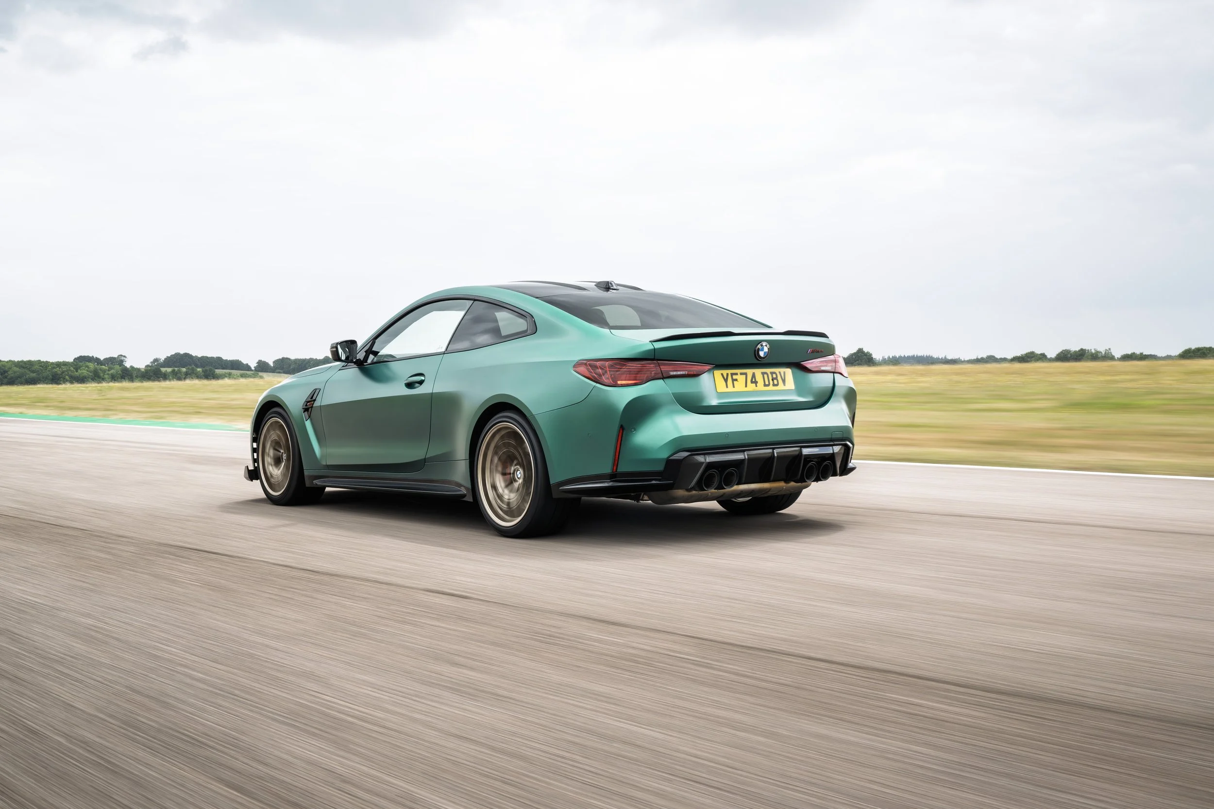Green BMW M4 sports car driving on a racetrack with a blurred background of sky and grass.
