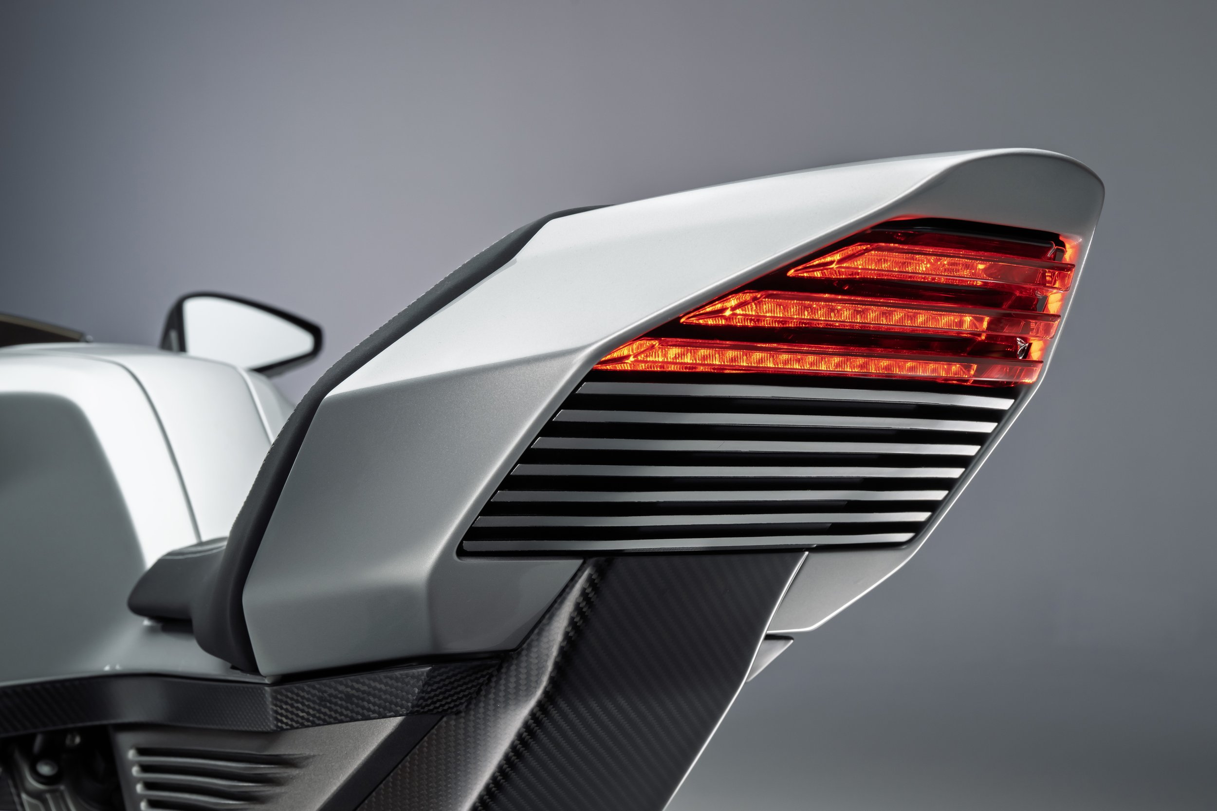 Close-up of a modern motorcycle's rear with red tail light and black vents, featuring sleek design and carbon fiber accents.