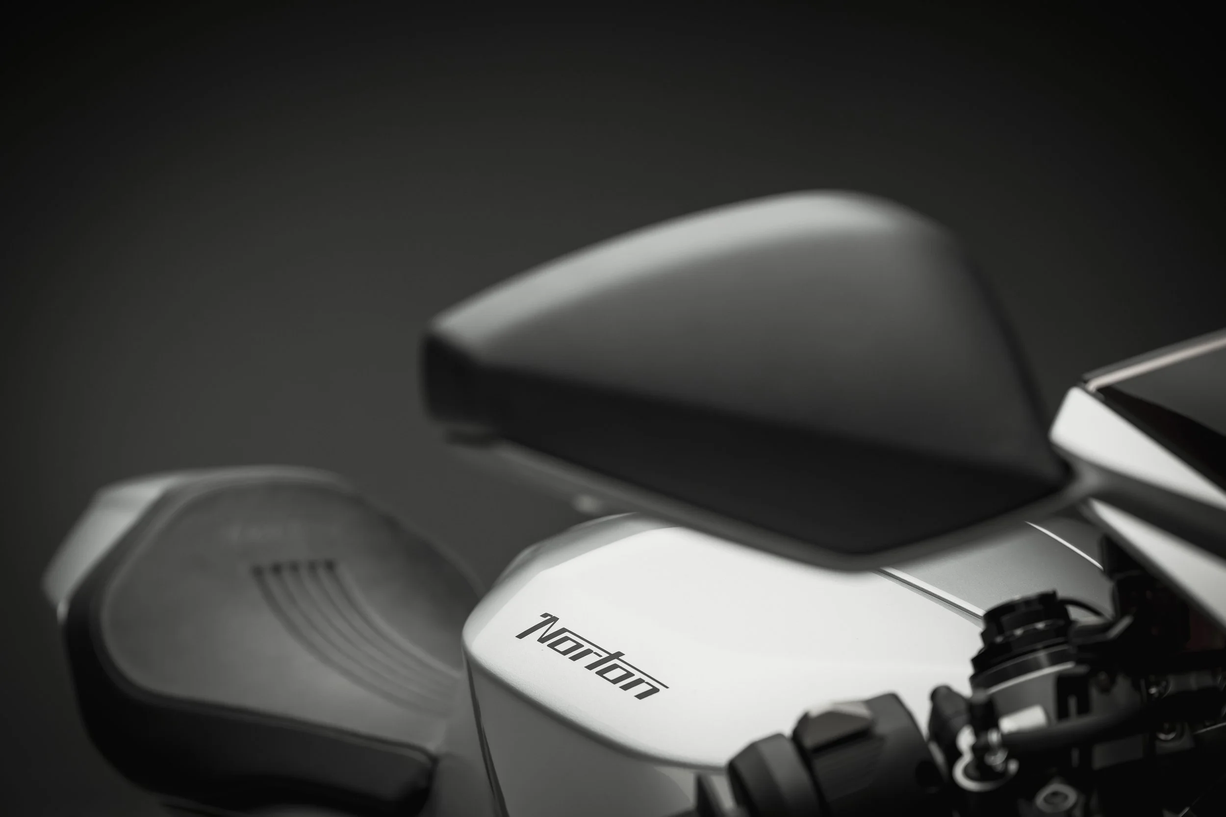 Close-up of a Norton motorcycle with focus on the seat and part of the body, against a dark background.